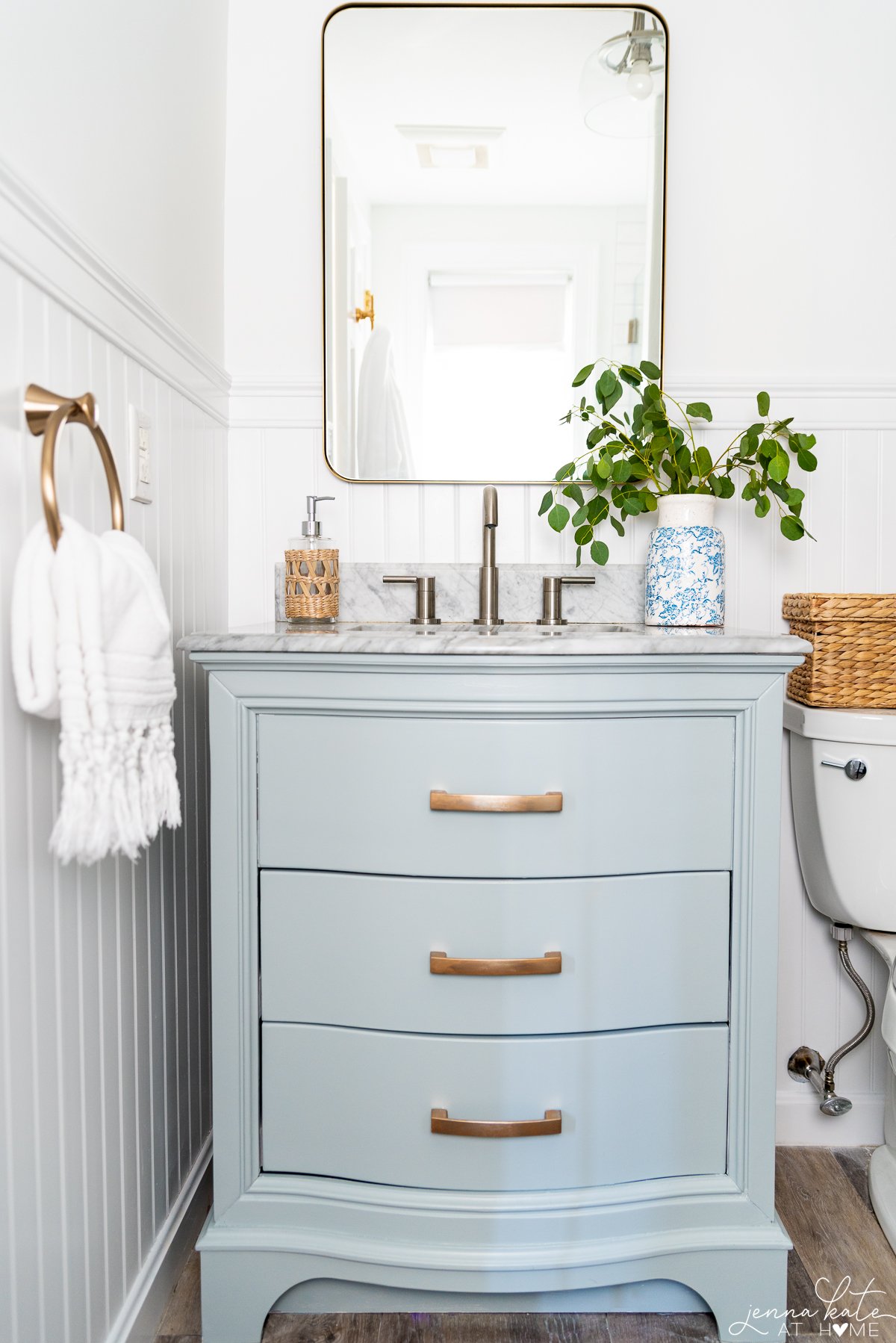 blue bathroom vanity with gold hardware and a vase of eucalyptus stems
