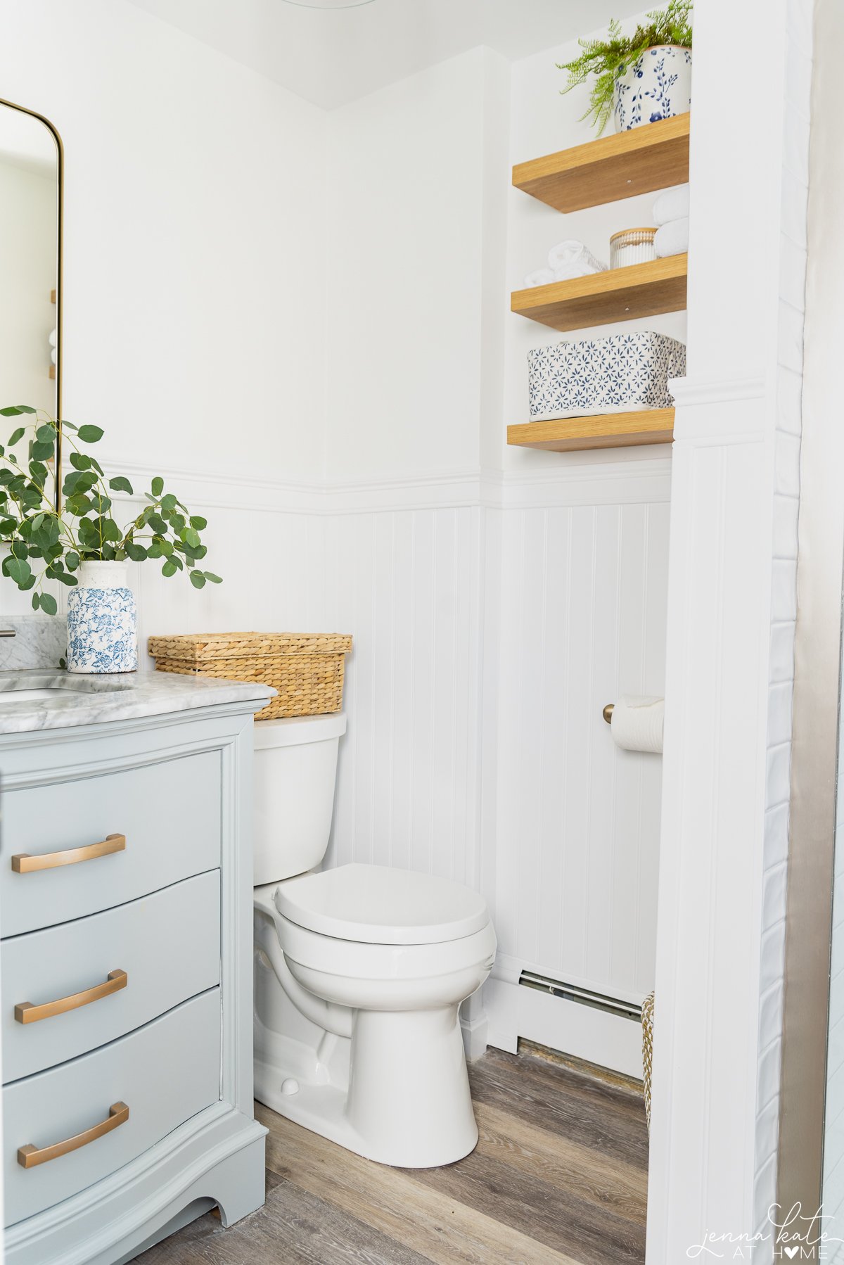 corner of a small bathroom with oak floating shelves and a toilet and vanity