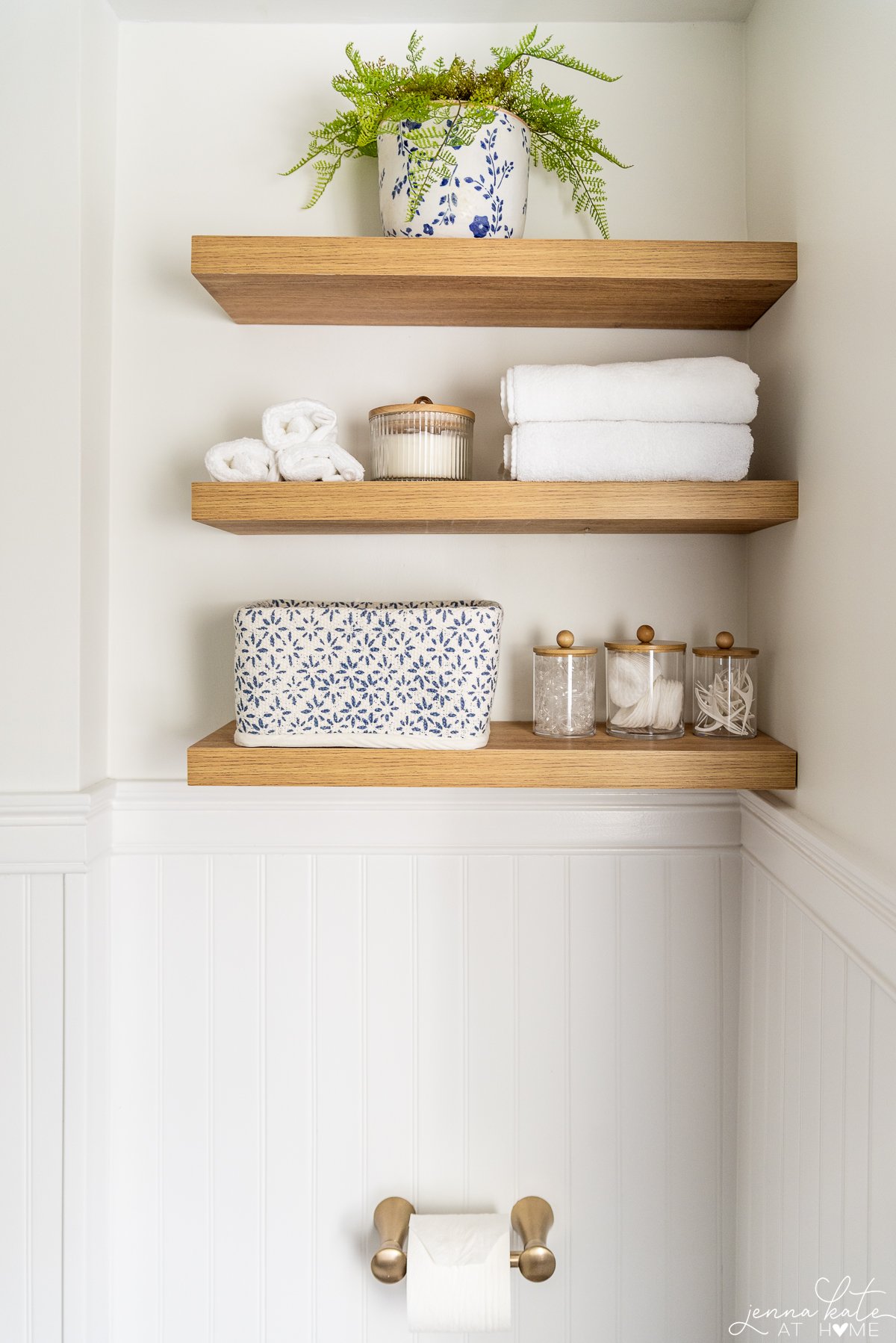 three white oak floating shelves in a bathroom with towels and storage items