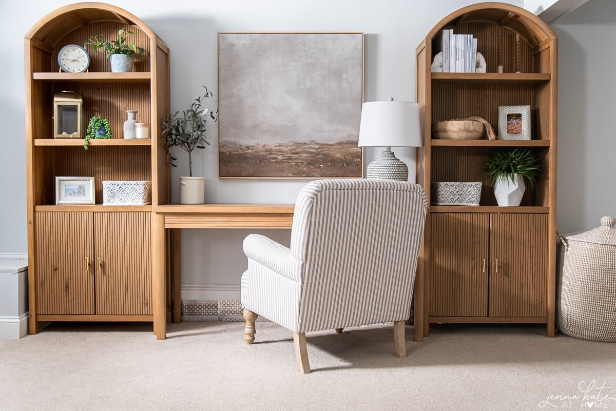 desk flanked by bookcases with art and a armchair in between