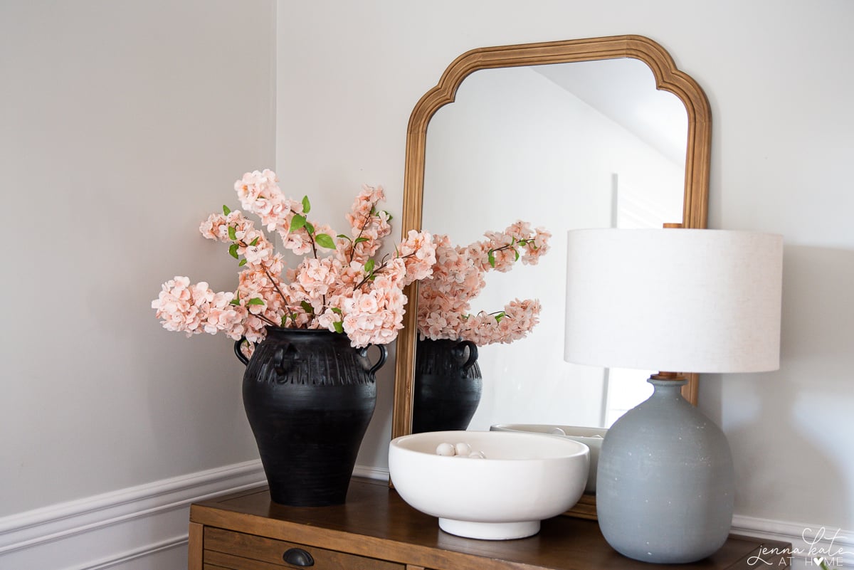console table with a lamp, mirror and black vase of fake cherry blossoms