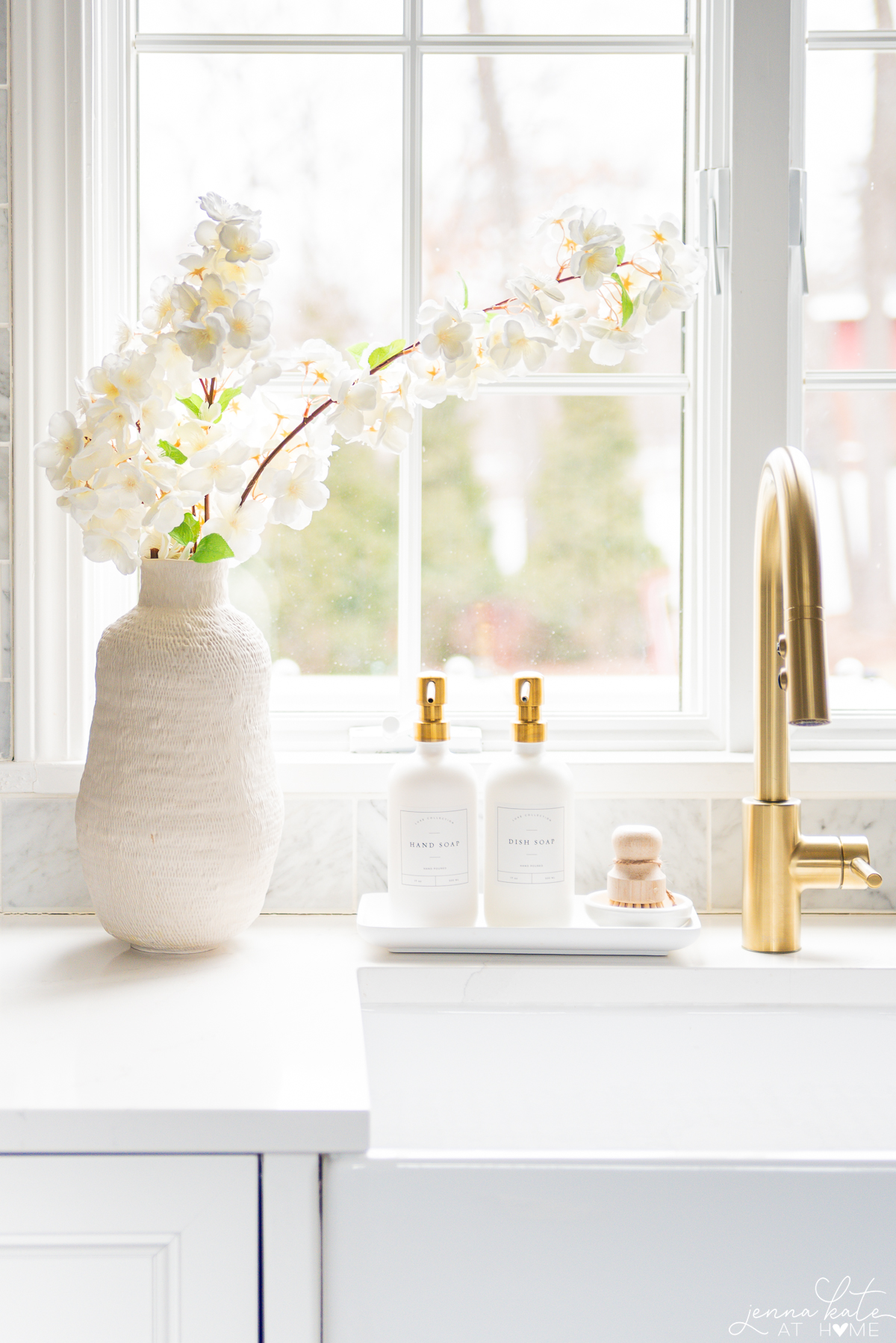 tall vase of faux cherry blossoms next to a sink.