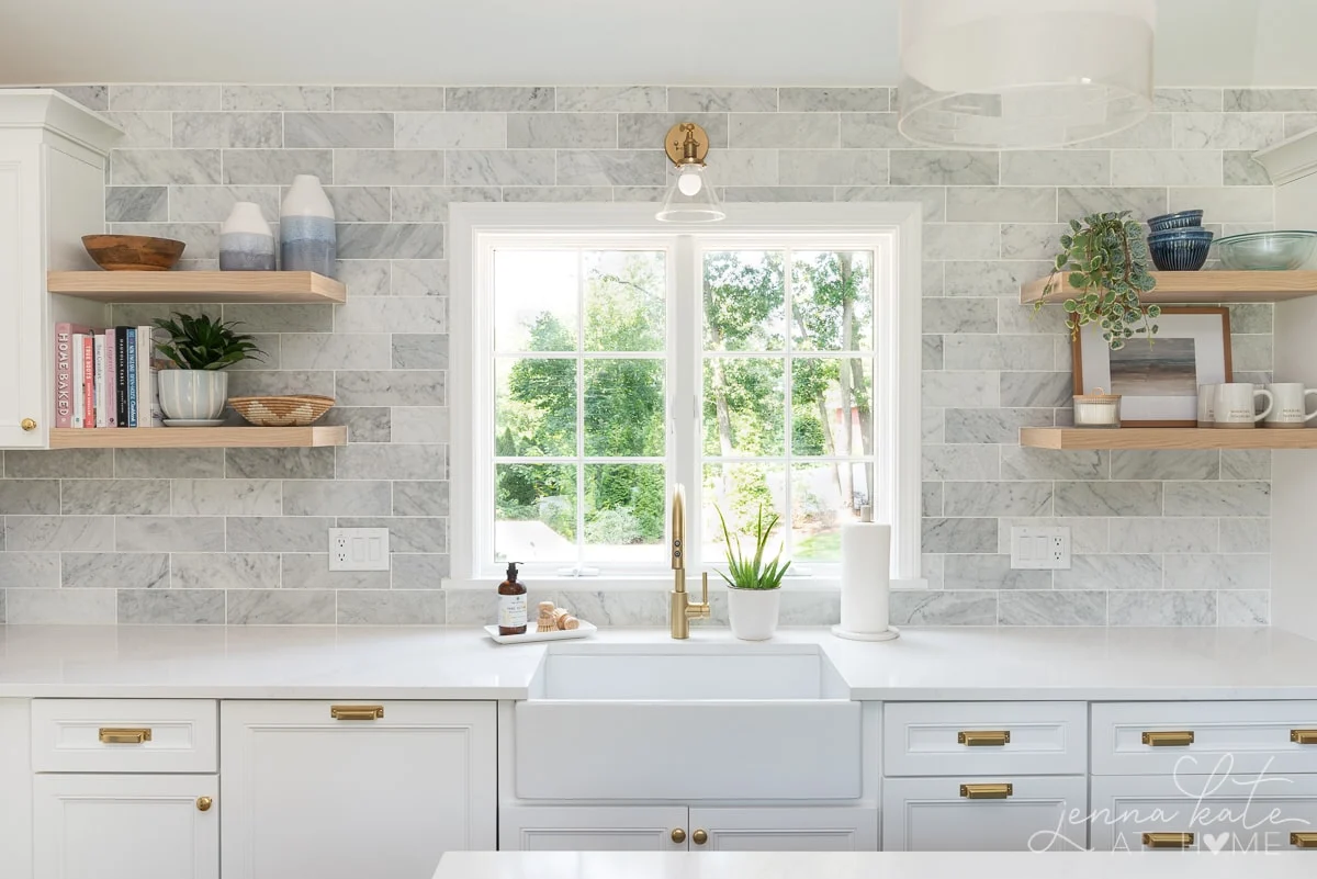 kitchen sink with window directly overhead and wooden floating shelves flanking