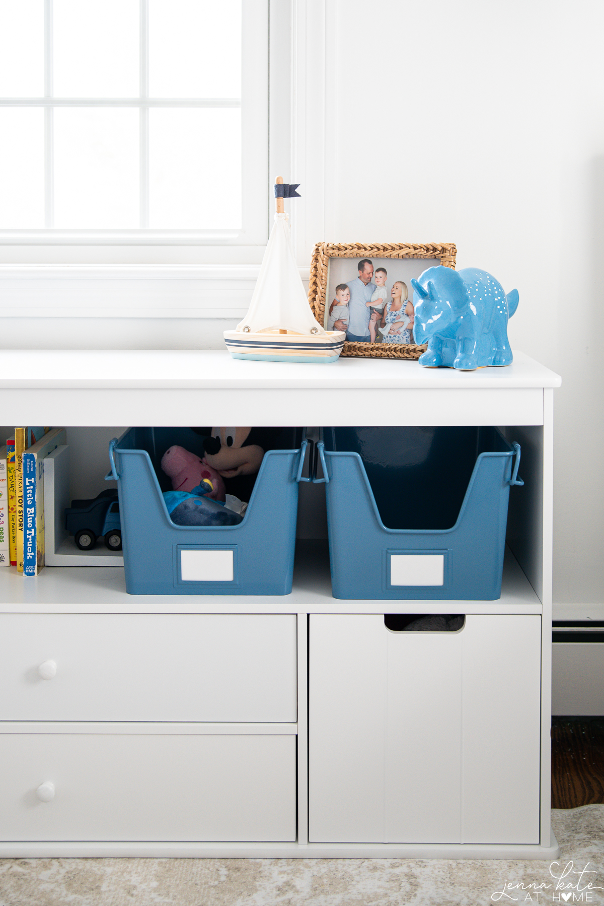 low bookcase with blue metal storage bins and a family photo and toy sailboat
