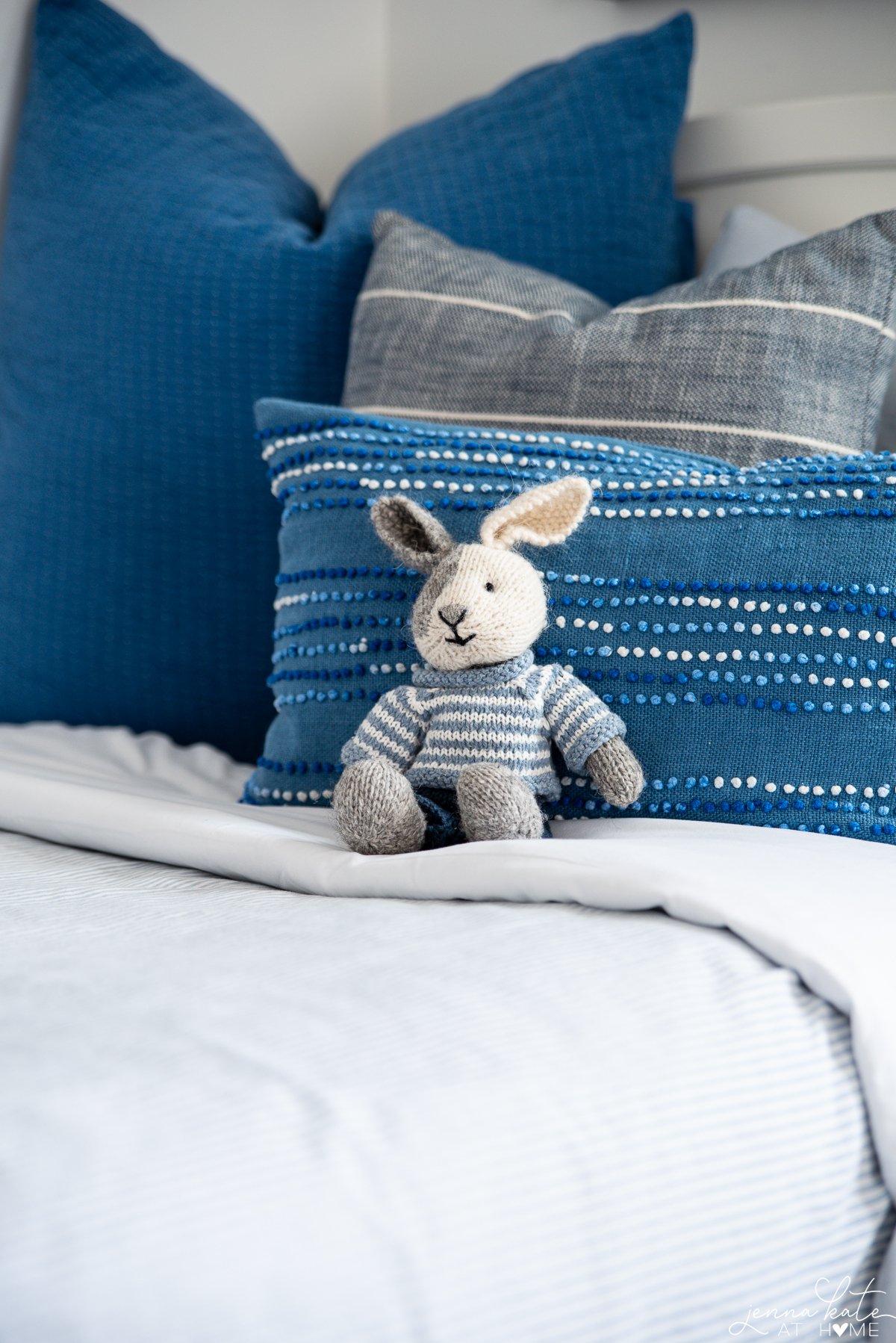 knitted bunny sitting on a bed with blue throw pillows
