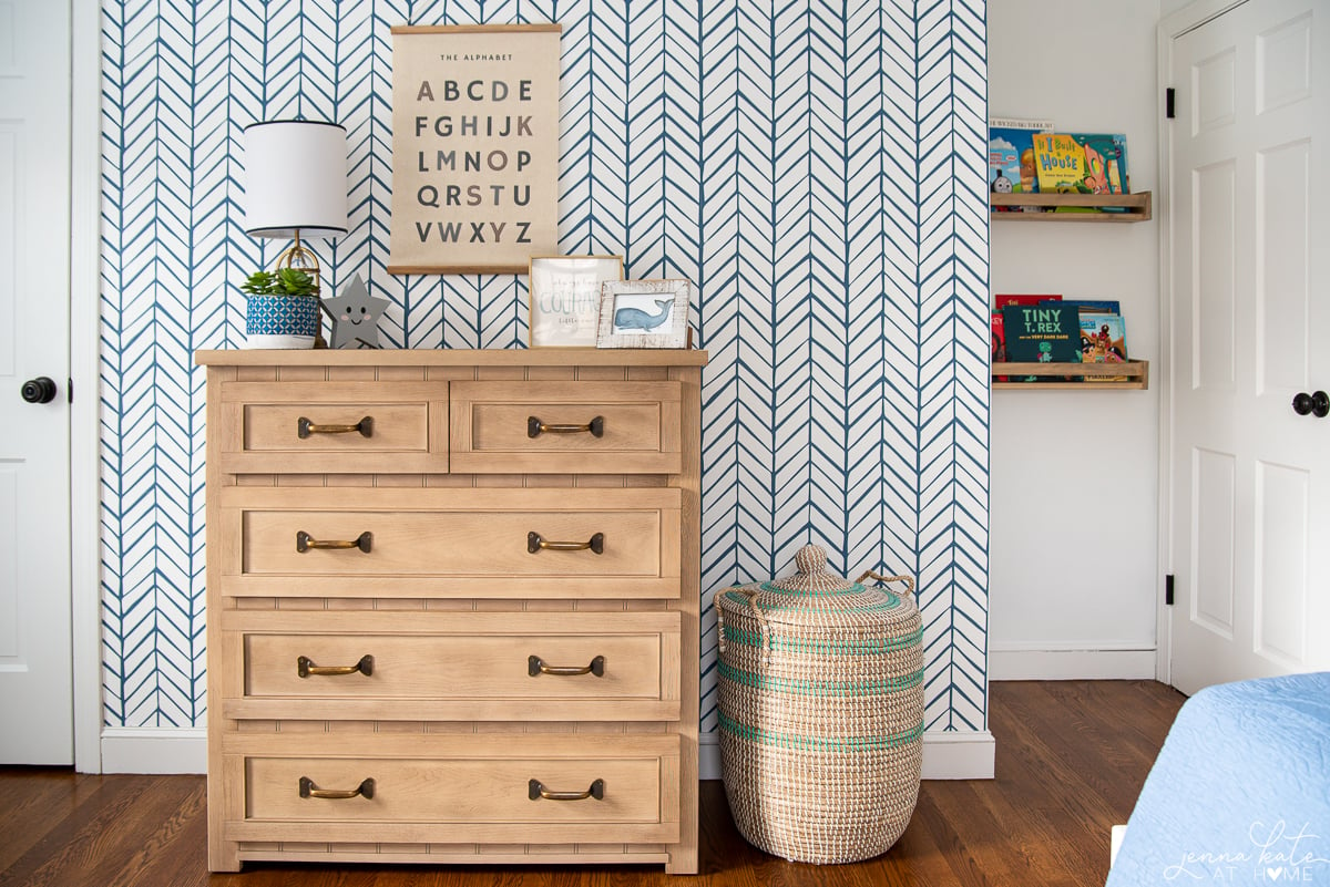 blue geometric wallpapered accent wall and a natural wood dresser