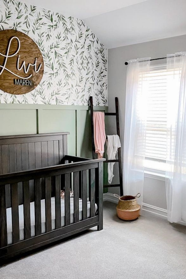 Nursery with sage green painted walls and floral wallpaper. 