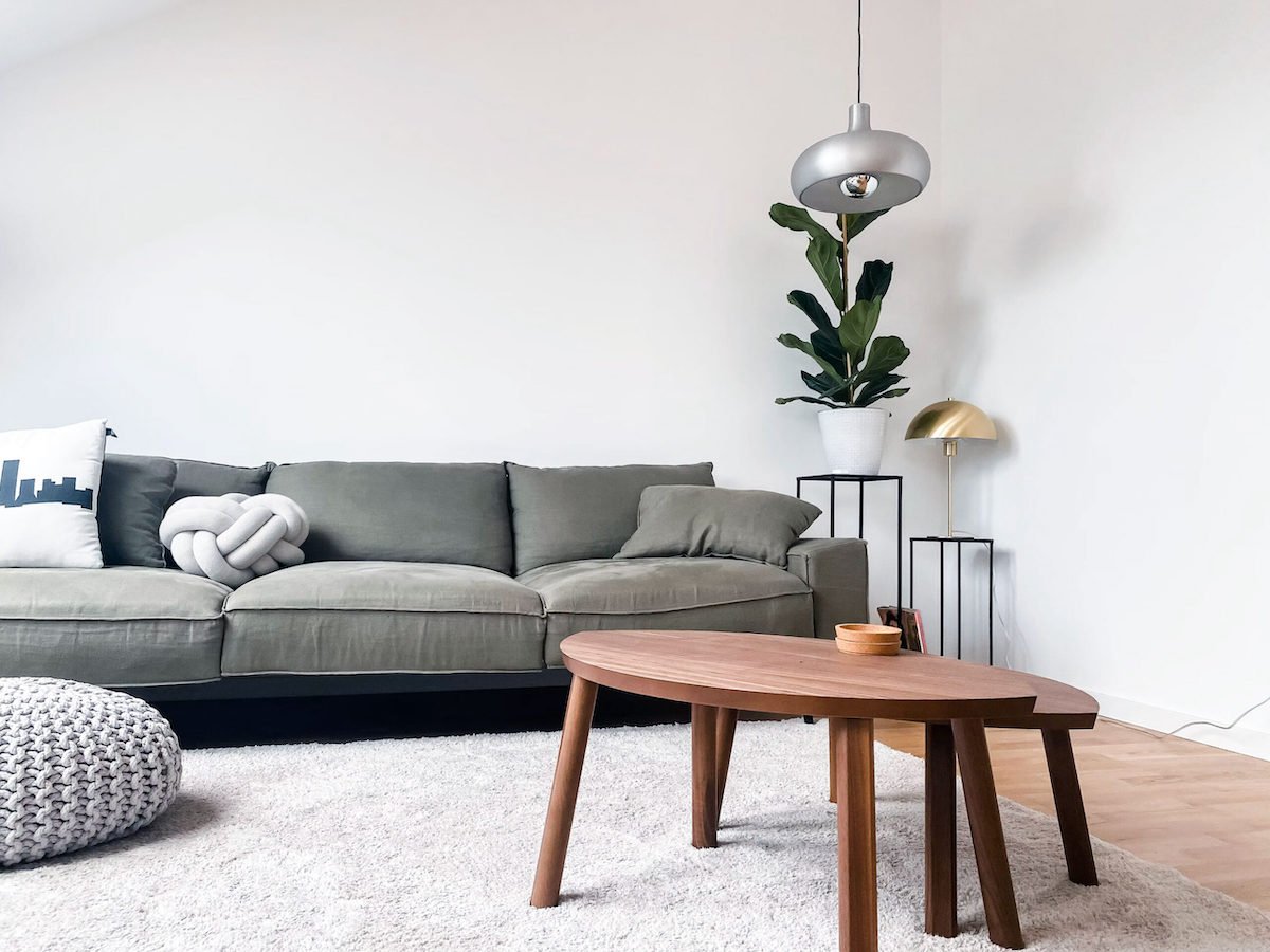 Living room painted with SW Natural White on the walls, a muted green sofa and wood coffee tables. 