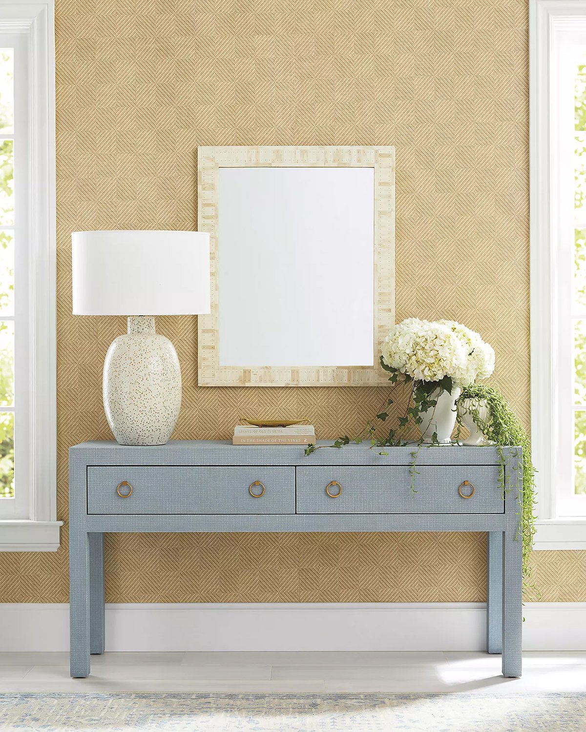 blue console table with rectangular mirror overhead, a vase on the left and flowers on the right