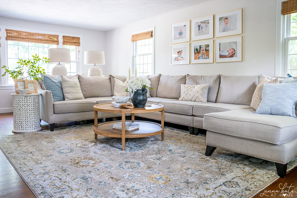 A living room with a sectional couch, coffee table in the middle, and side table beside couch. A gallery wall of 6 pictures hangs overhead.