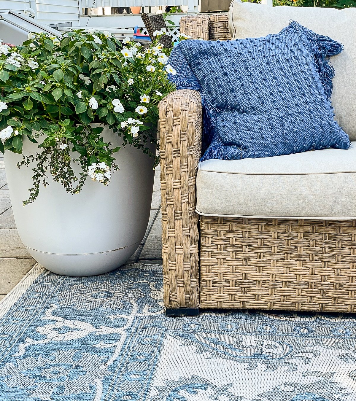 corner of the outdoor couch with a blue throw pillow and a planter of white flowers next to it