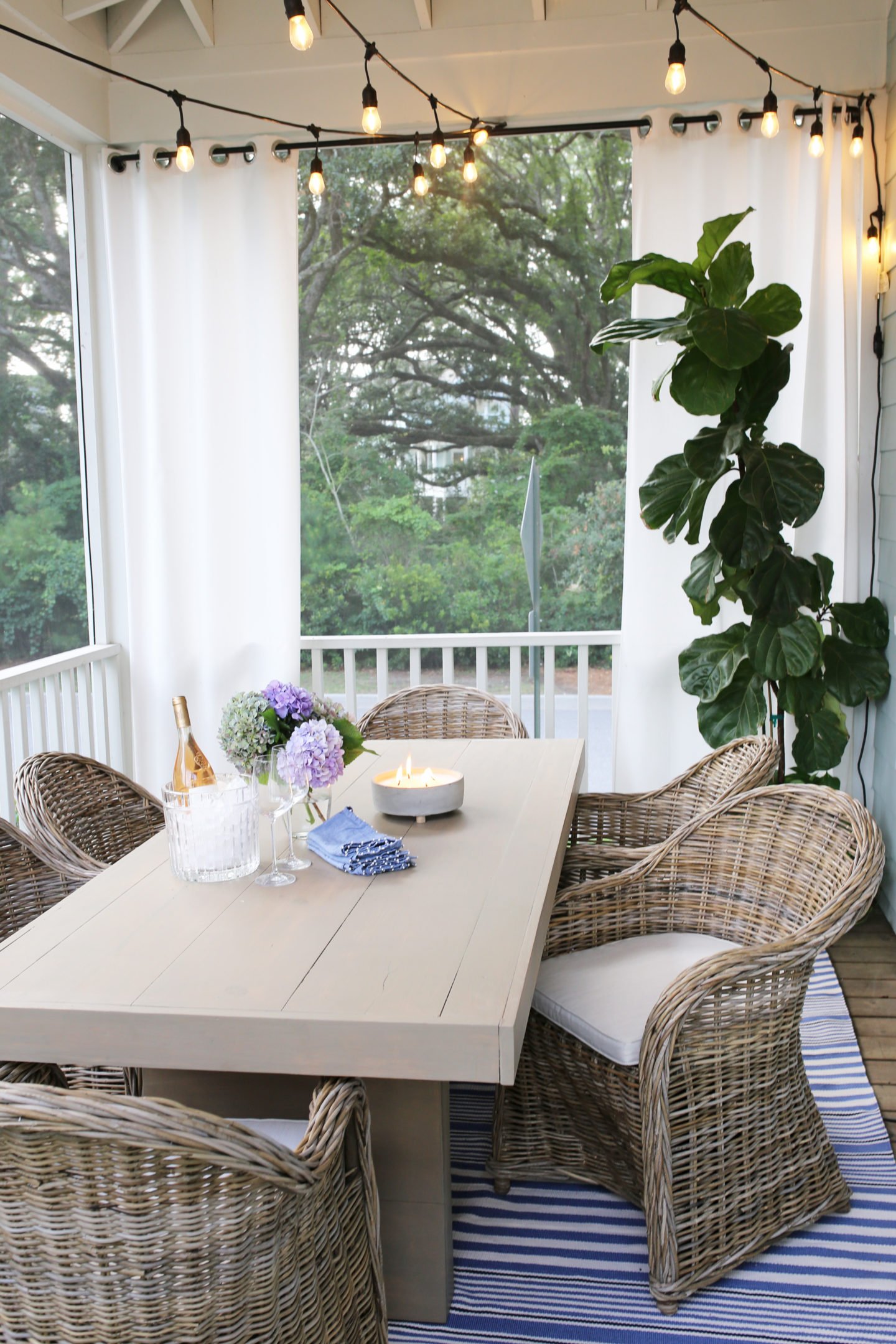 Screened porch with dining table, rattan chairs and string lights overhead