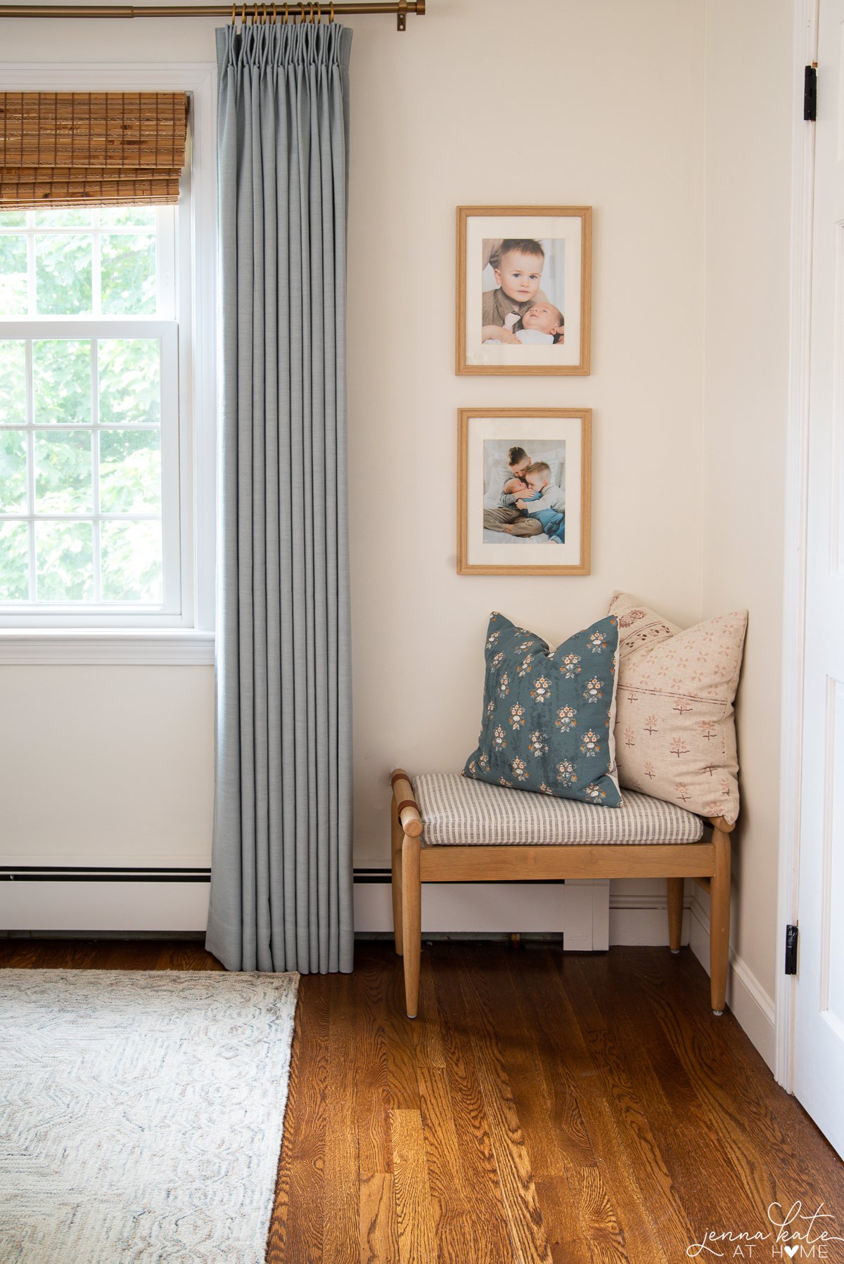 corner of a bedroom with small bench with throw pillows and blue curtains on the window