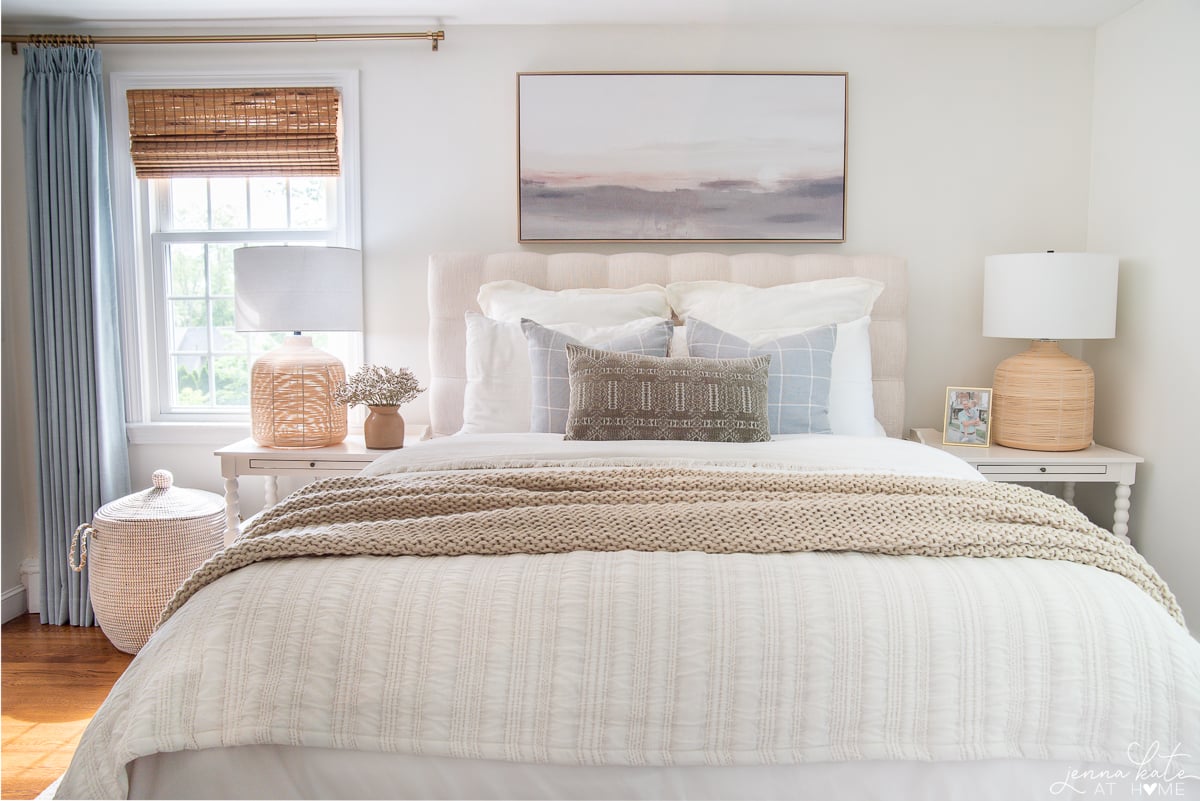 bed with white bedding and throw pillows flanked by white nightstands with rattan table lamps