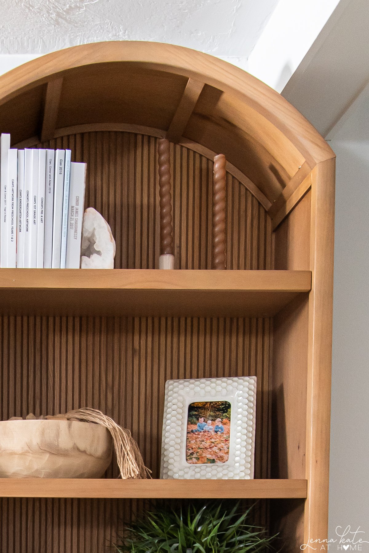 Two candles in candle holder on the top shelf of a bookcase