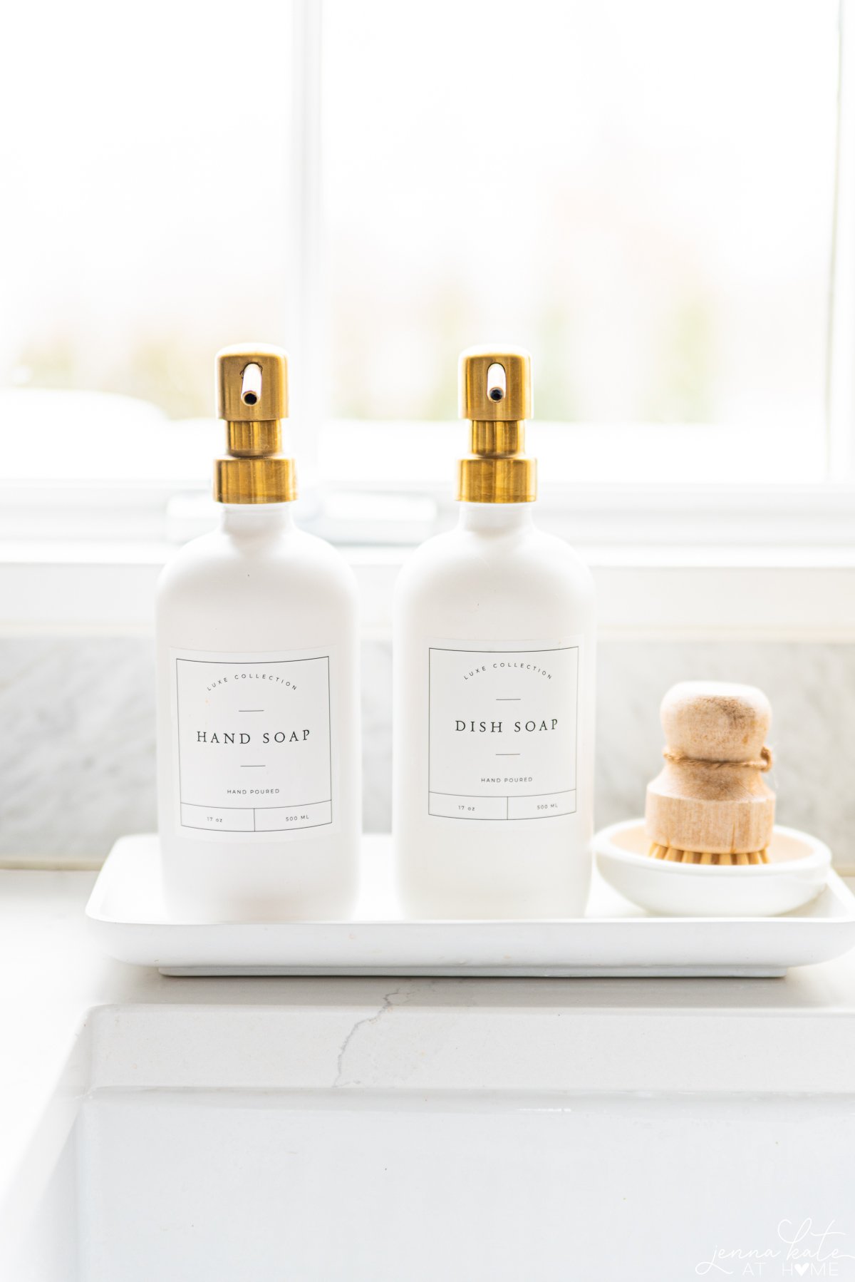 White glass bottles for hand soap and dish soap sitting next to a kitchen sink