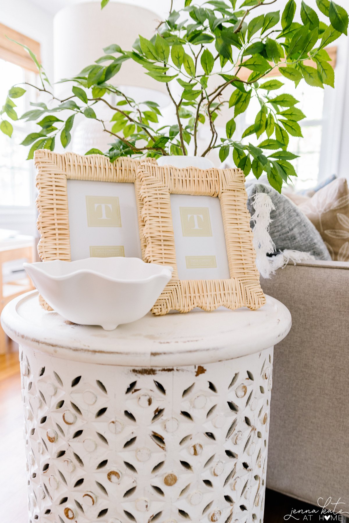 end table with scalloped rattan picture frames and green leafy stems in a vase