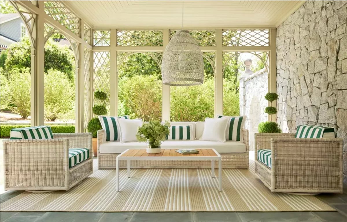 An outdoor patio with a pendant light and patio furniture. A dark green and white striped color pattern with accent pillows and a striped rug.