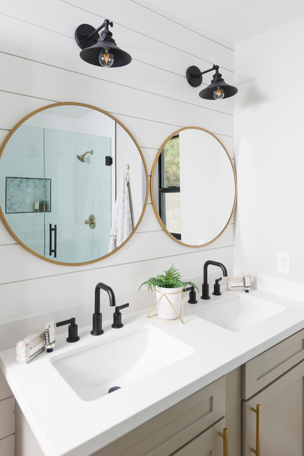 shiplap bathroom with round gold mirror, black faucets and black lights