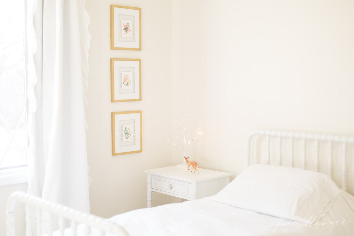Little girl's bedroom with white bed and nighstand and 3 stacked photos on the wall