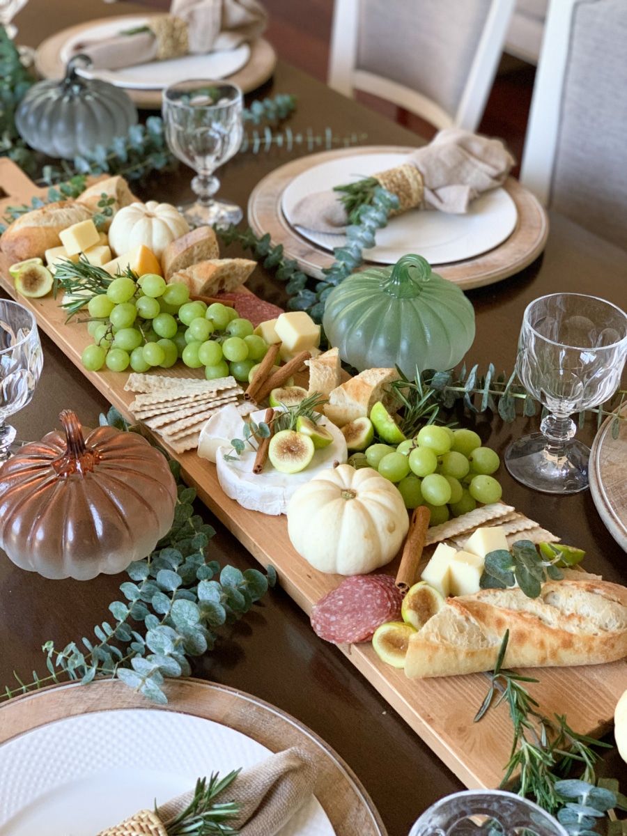 Elegant charcuterie board centerpiece with eucalyptus leaves and glass pumpkins around it
