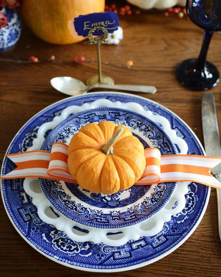 Blue and white intricate detailed plate settings with miniature orange pumpkin and orange and white ribbon