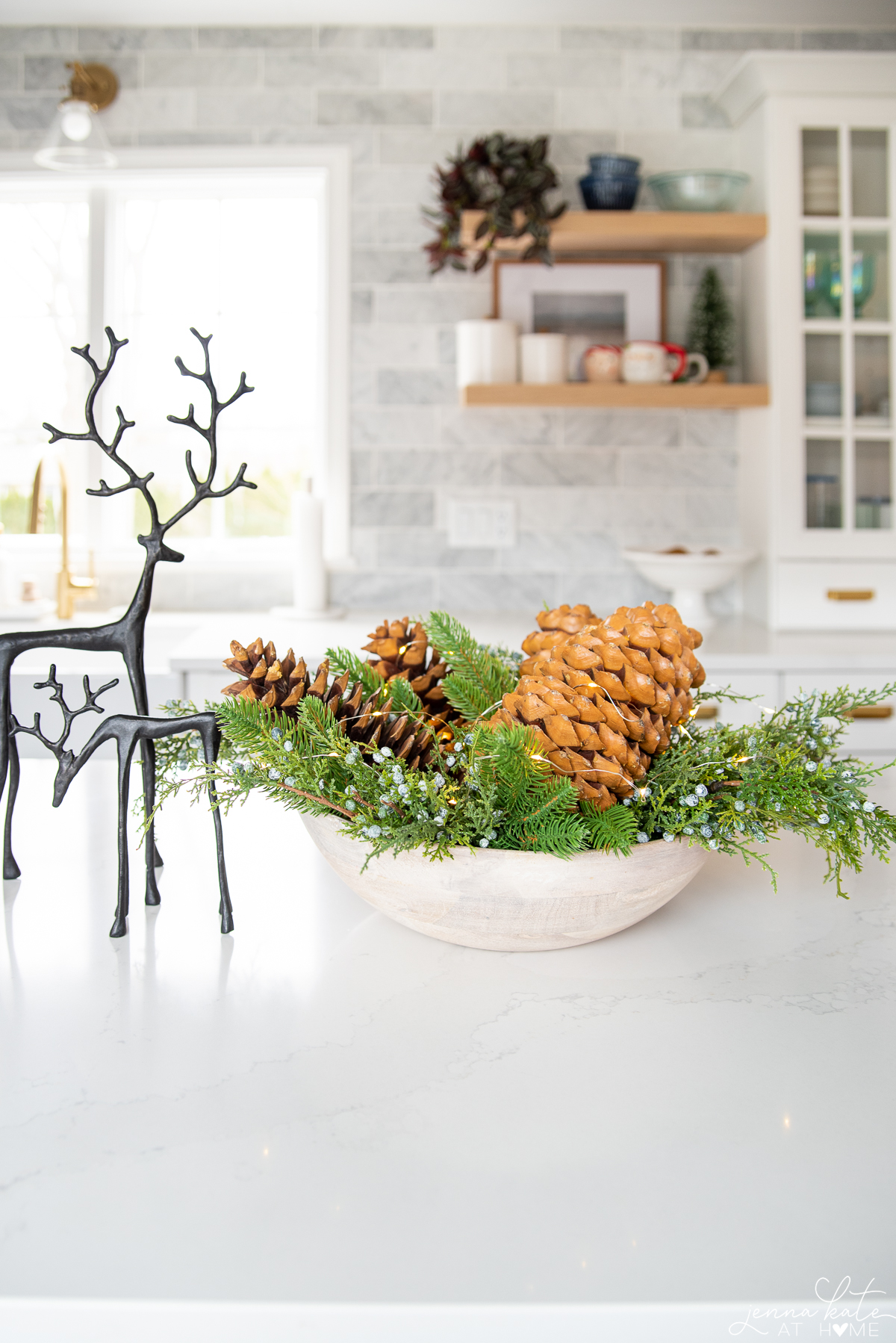 a centerpiece display including a bowl filled with greenery and pine cones and a couple of fake deer statues