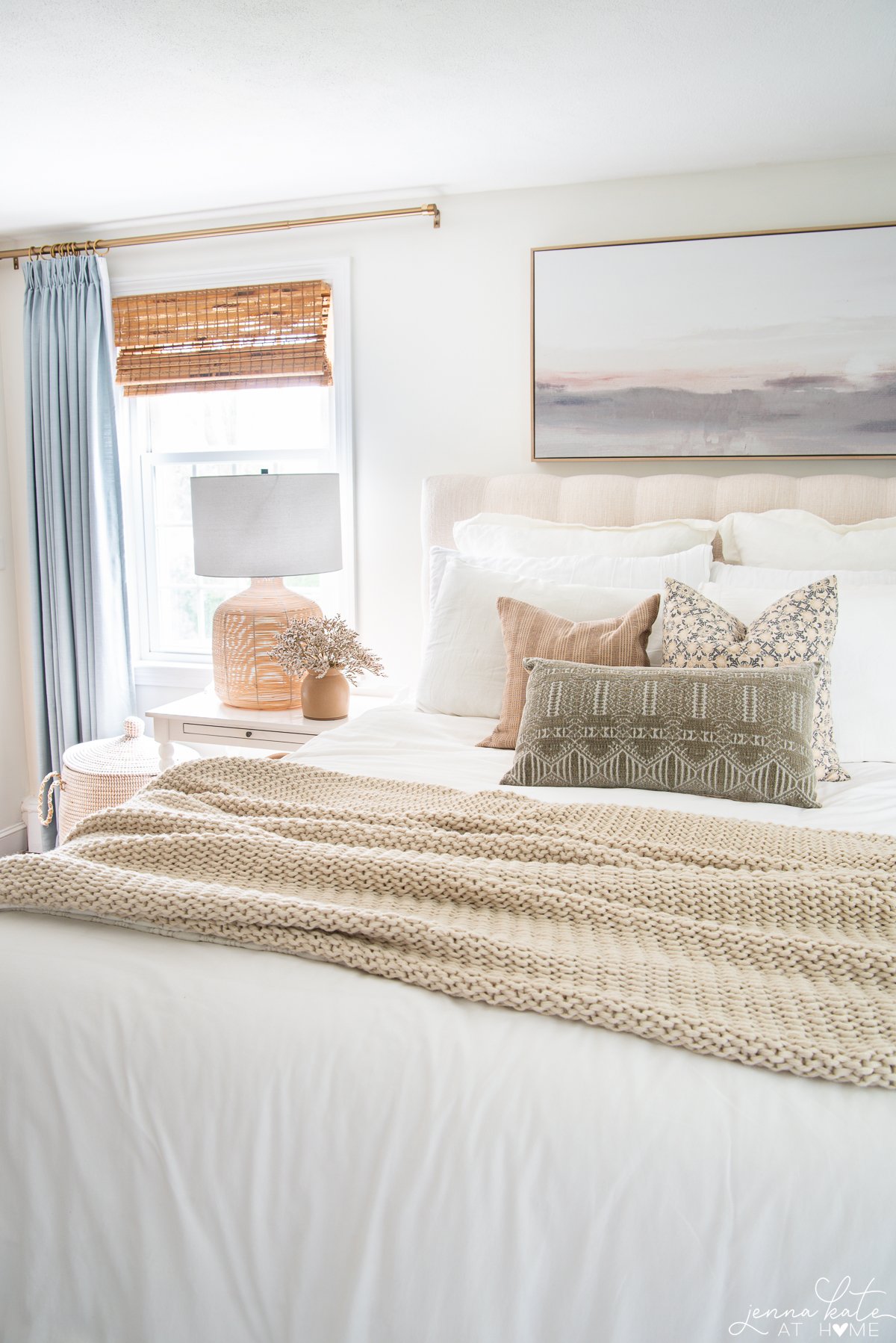 bedroom with a bed with white bedding, art over the bed and neutral throw pillows.