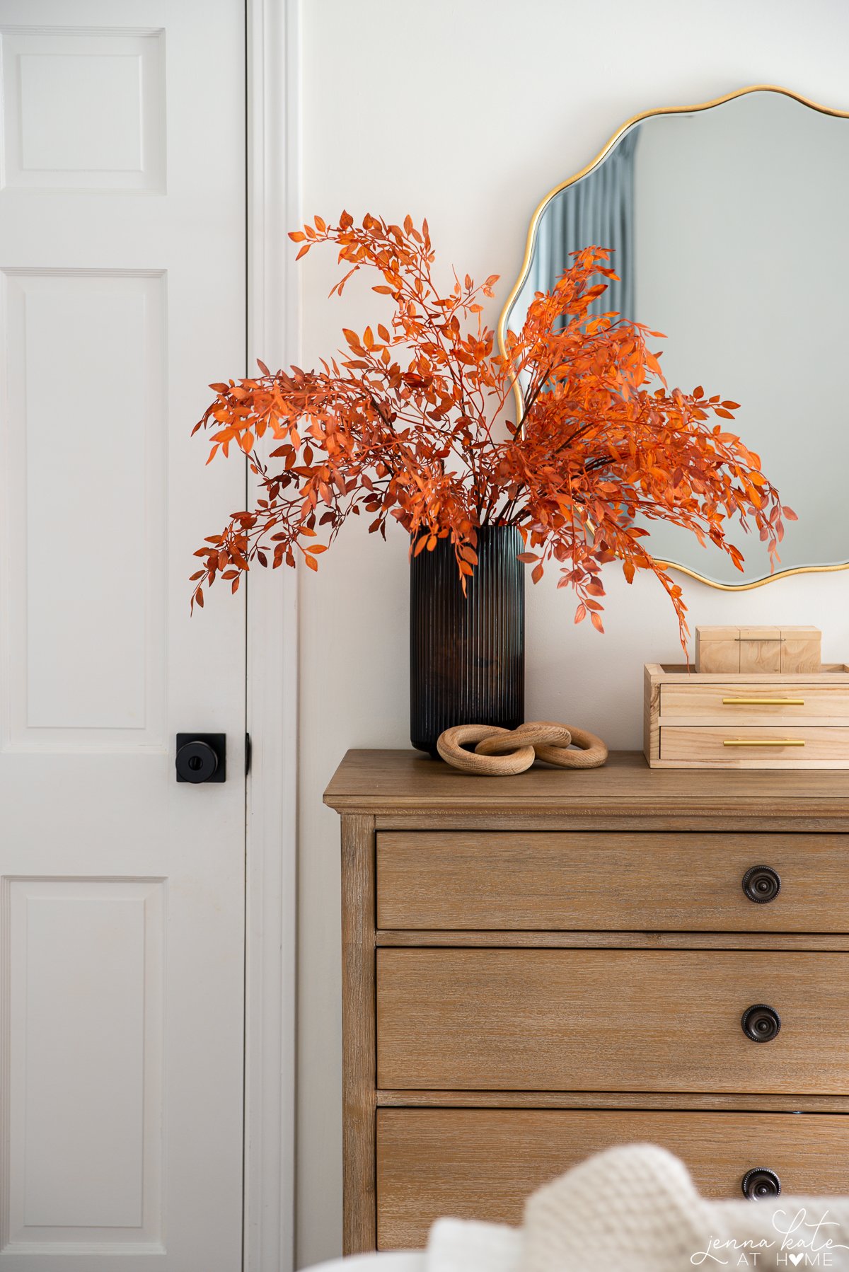 wooden dresser with orange fall stems in a glass vase.