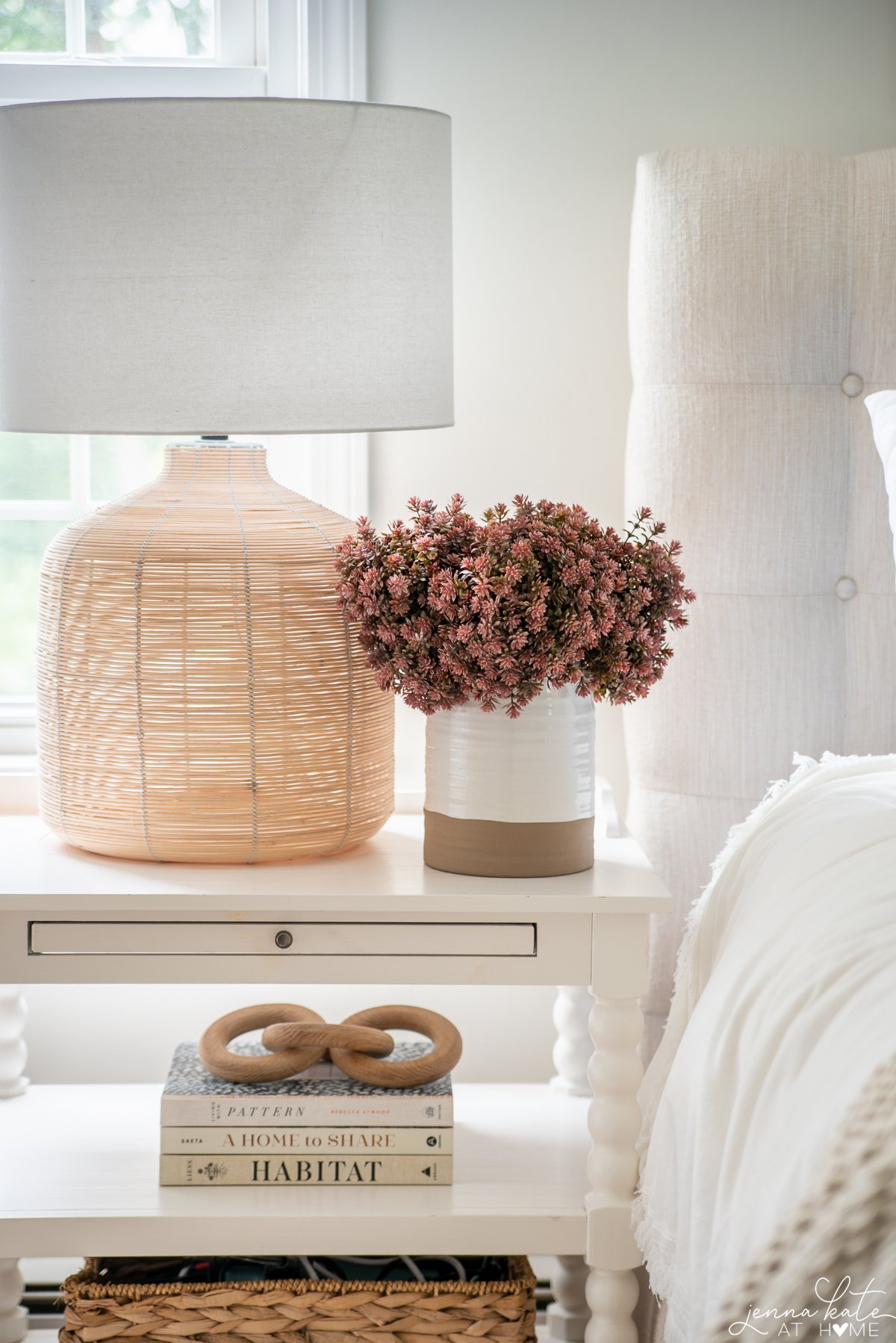 nightstand with a rattan lamp and a vase filled with faux sedum.