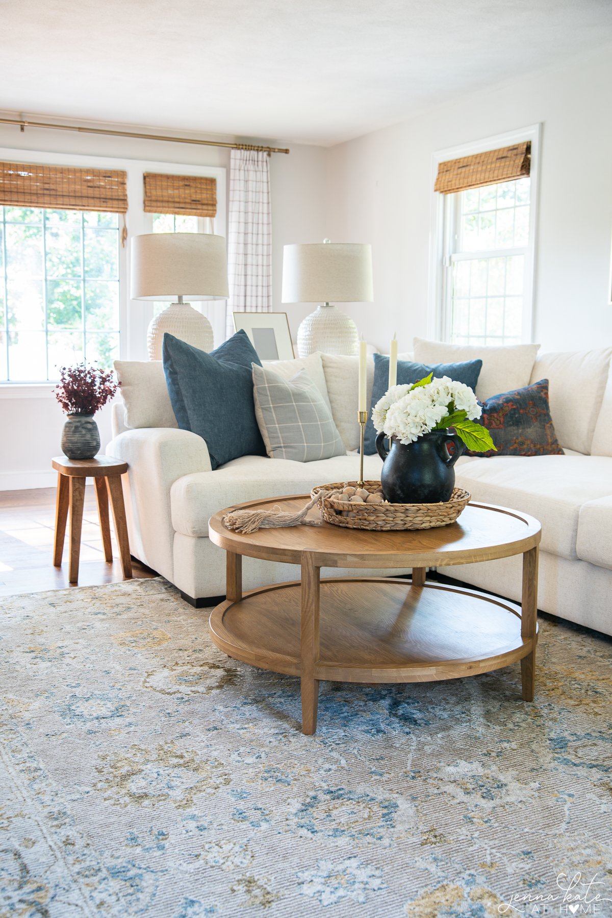 Living room decorated for fall with blue and white pillows, faux plants, and white natural lamps.