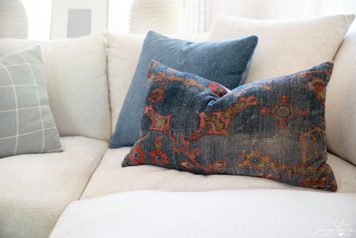 Throw pillow display on sofa featuring a solid blue pillow, solid cream pillow, blue and red patterned pillow, and a sage green striped pillow.