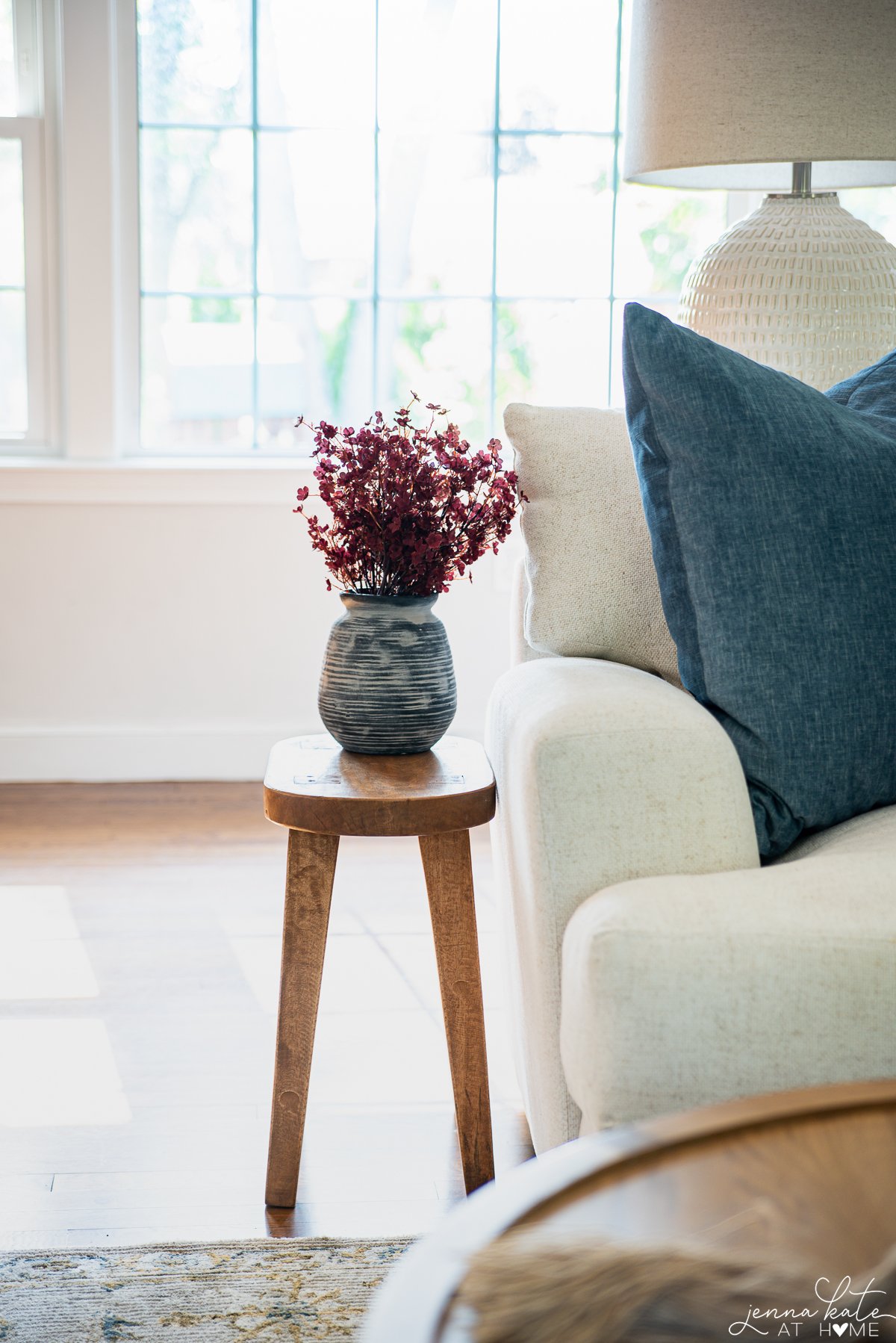 Faux Burgundy leaves in a deep blue vase displayed on a corner table next to the sofa.