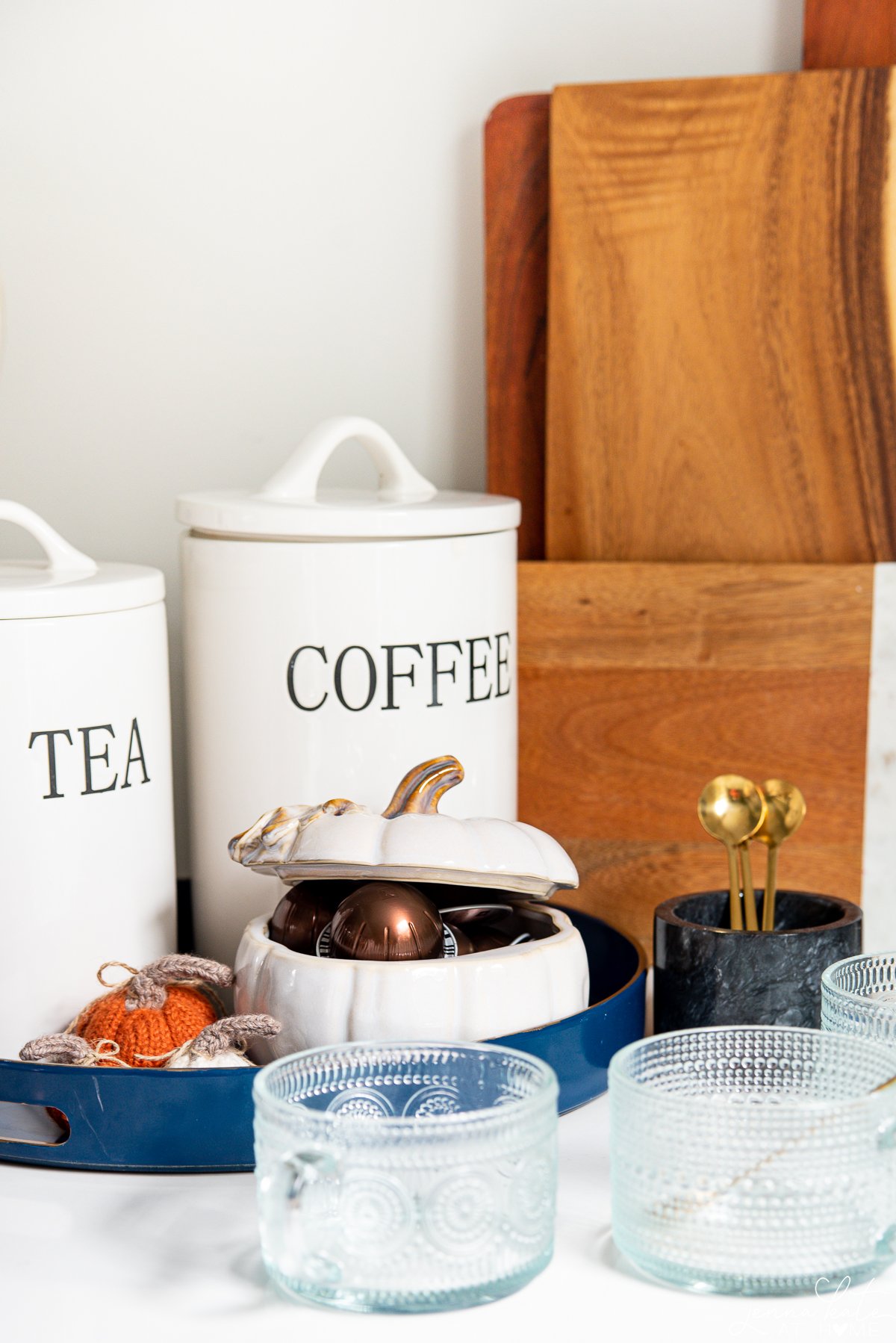 fall-themed coffee station with pumpkin filled with coffee pods, glass mugs and tea and coffee canisters