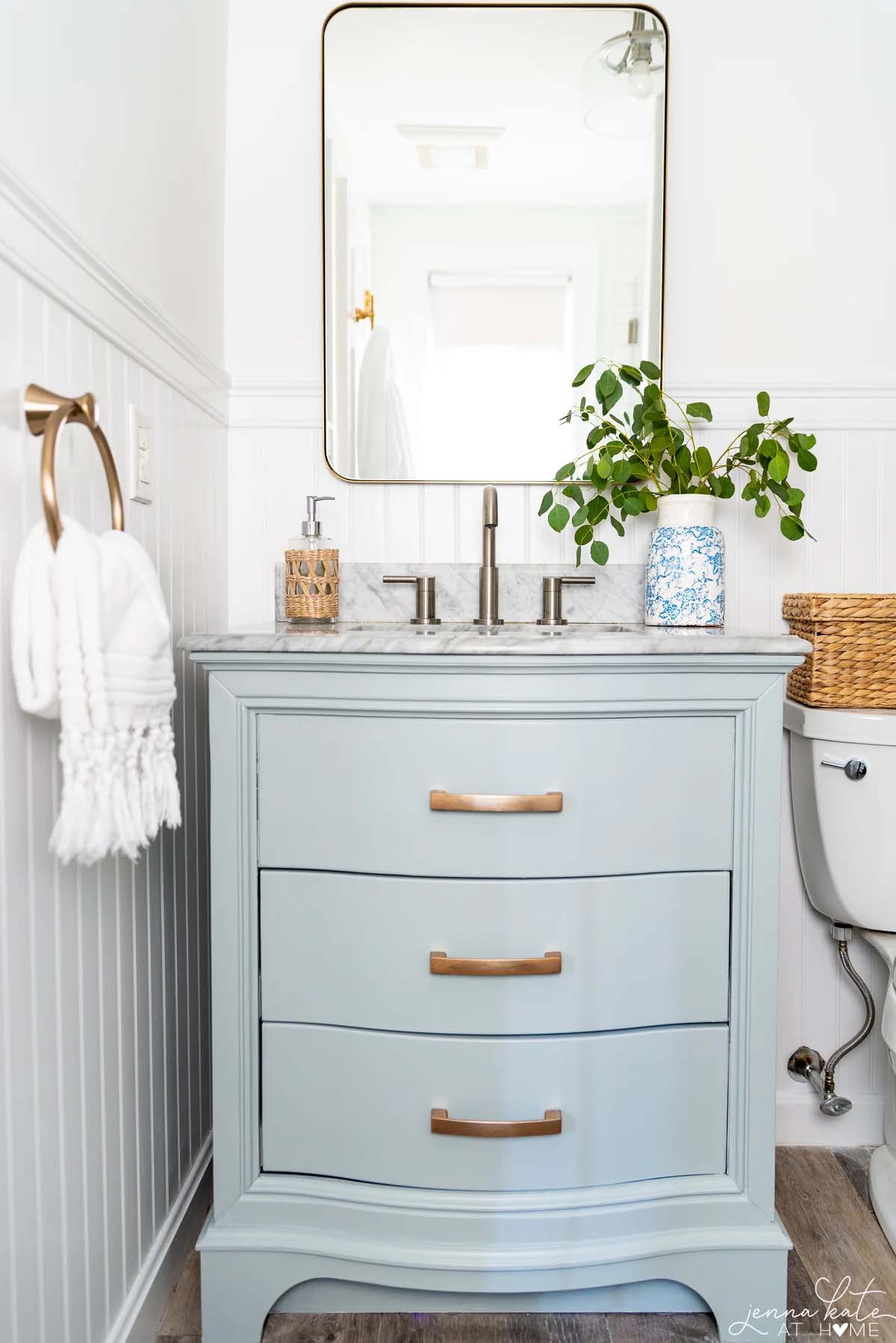 freshly painted bathroom vanity cabinet in a light blue color with marble top and brass mirror above it