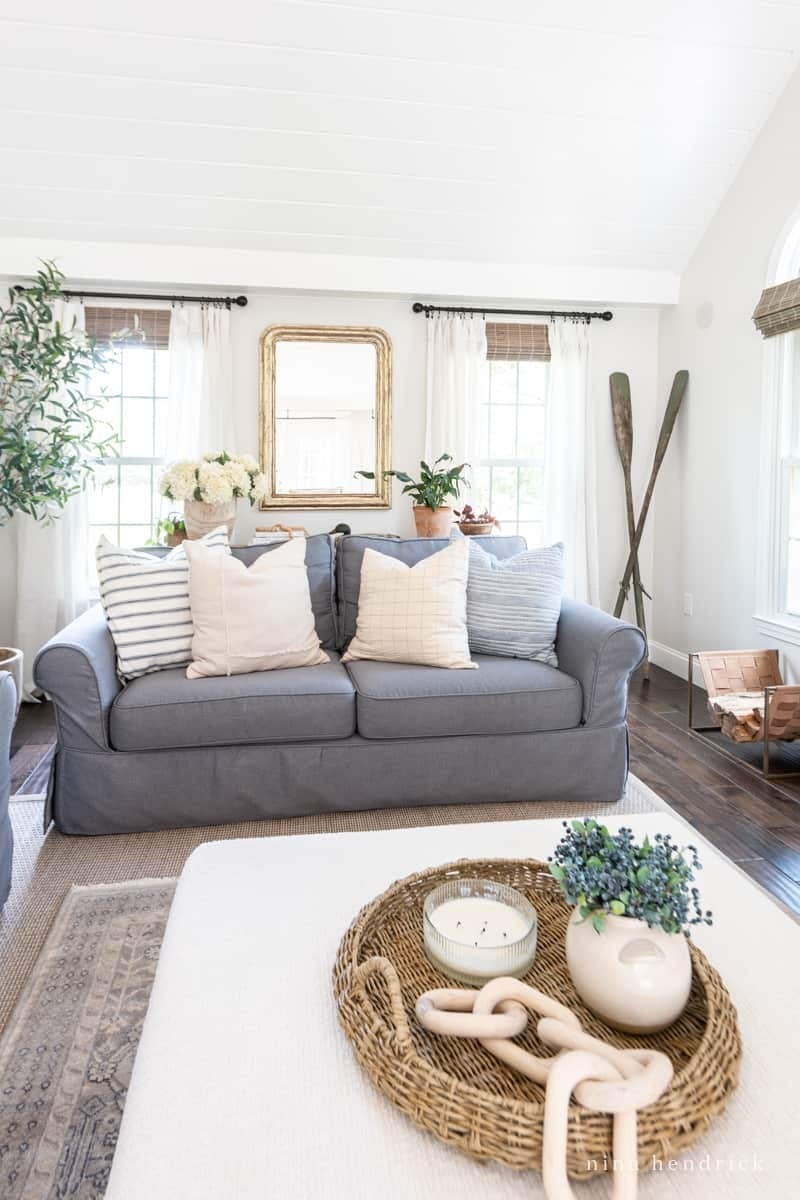 Couch with a slipcovers featured in a styled living room with decorative throw pillows, a coffee table, and a large mirror hanging overhead.