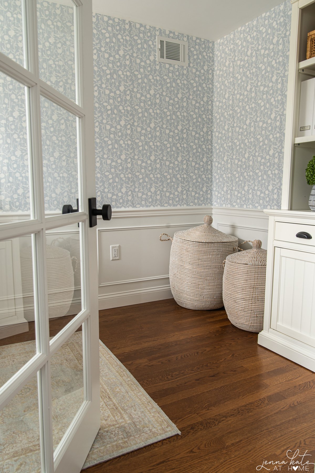 room with warm wood floors, white wainscoting and blue floral wallpaper