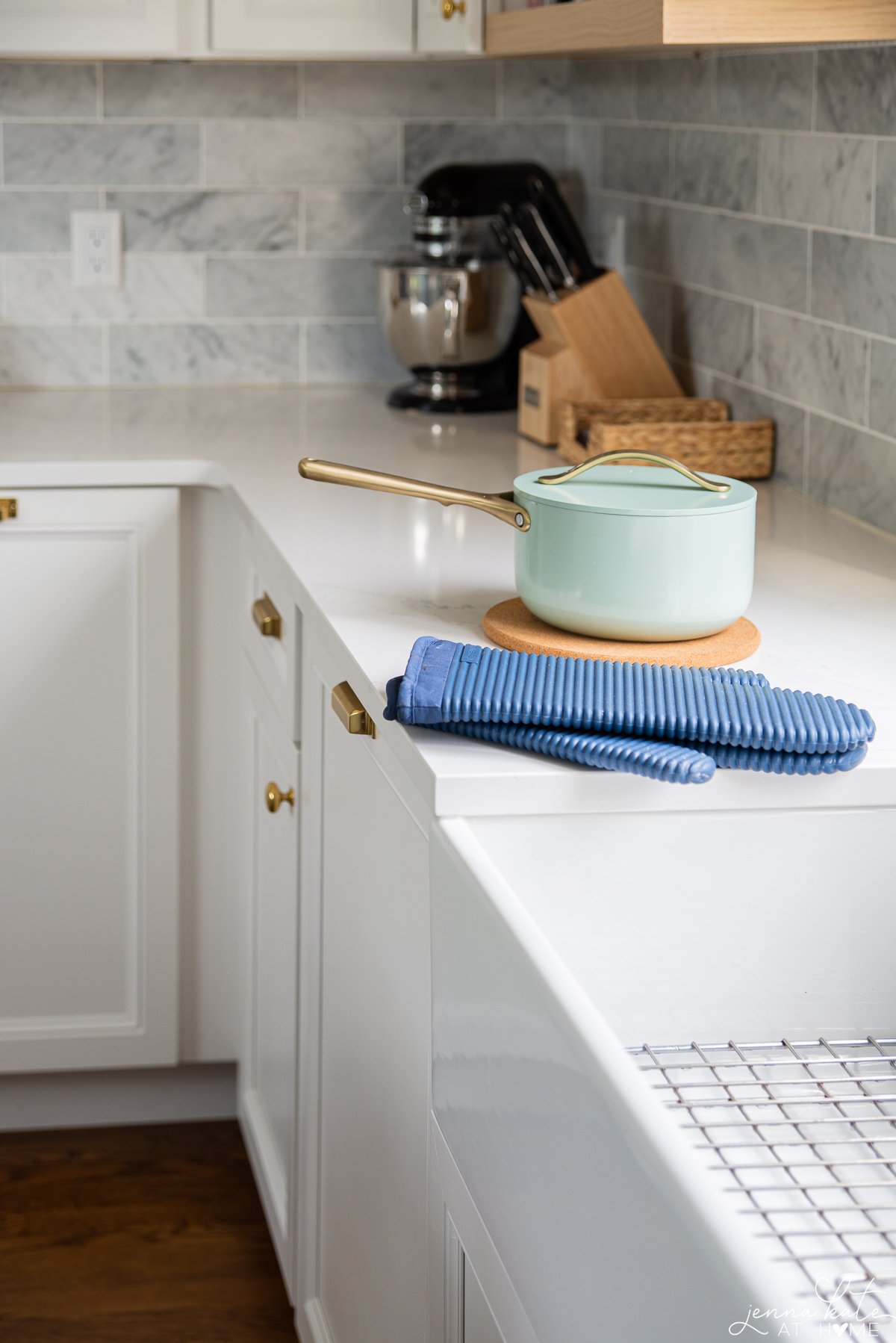 hot pot on a cork trivet with blue oven gloves sitting on the white quartz countertop