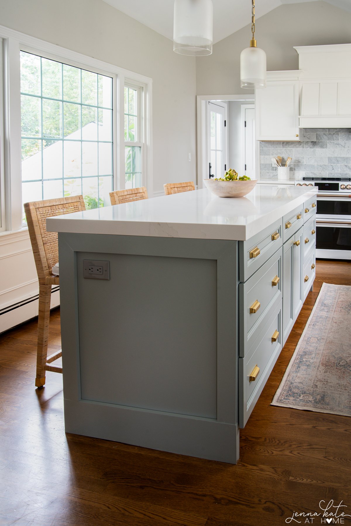 blue gray island with white quartz countertops and wooden bowl of fruit in the center