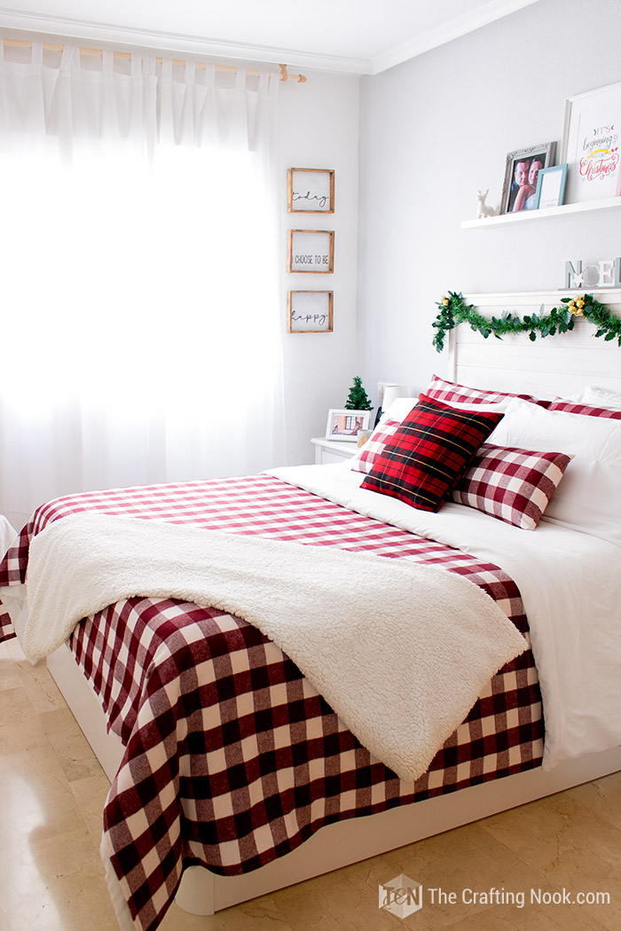 Plaid bedspread with white throw blankets and pillows.