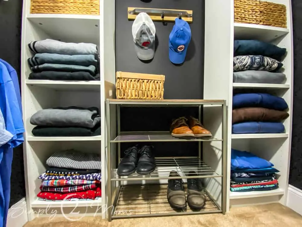 Closet with two storage shelves and a shoe rack in the middle. Hooks hanging overhead to store hats.