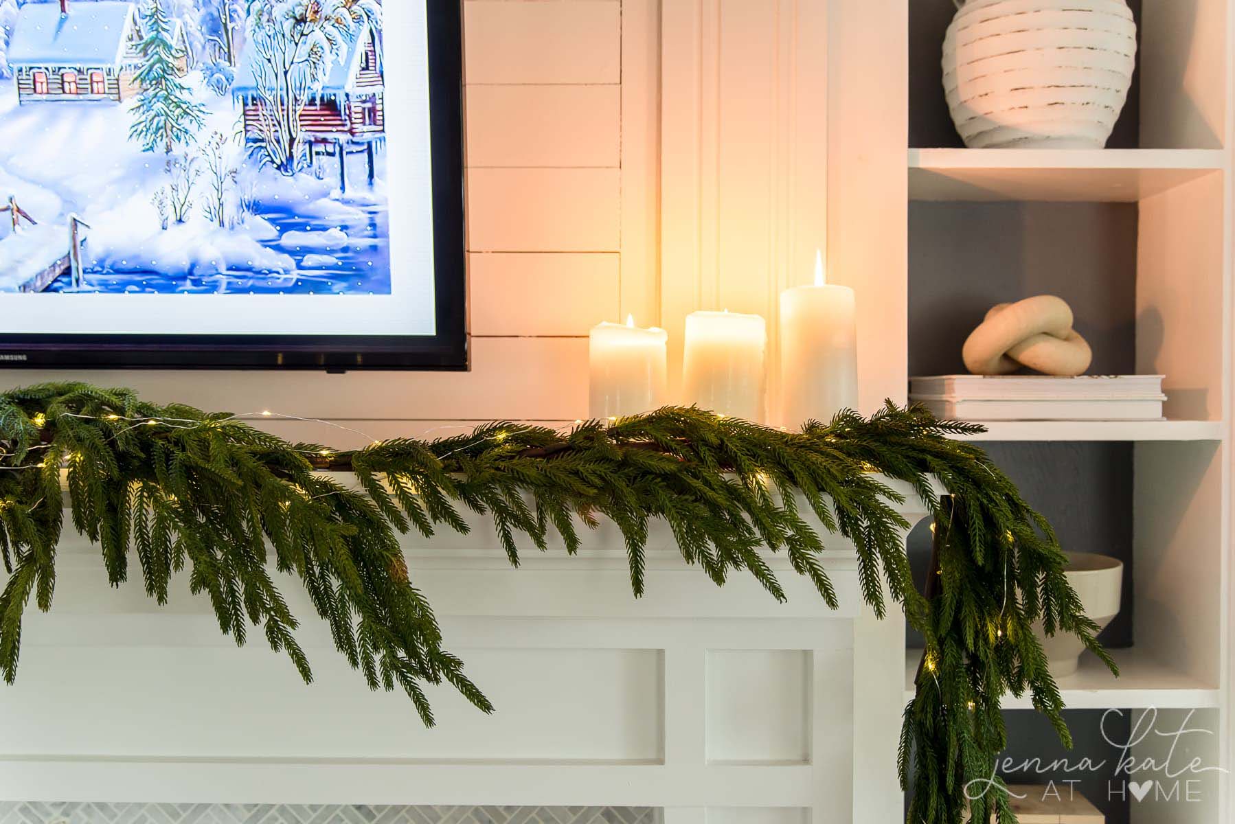 artificial pine garland on a mantel with string lights and 3 candles lit on the mantel