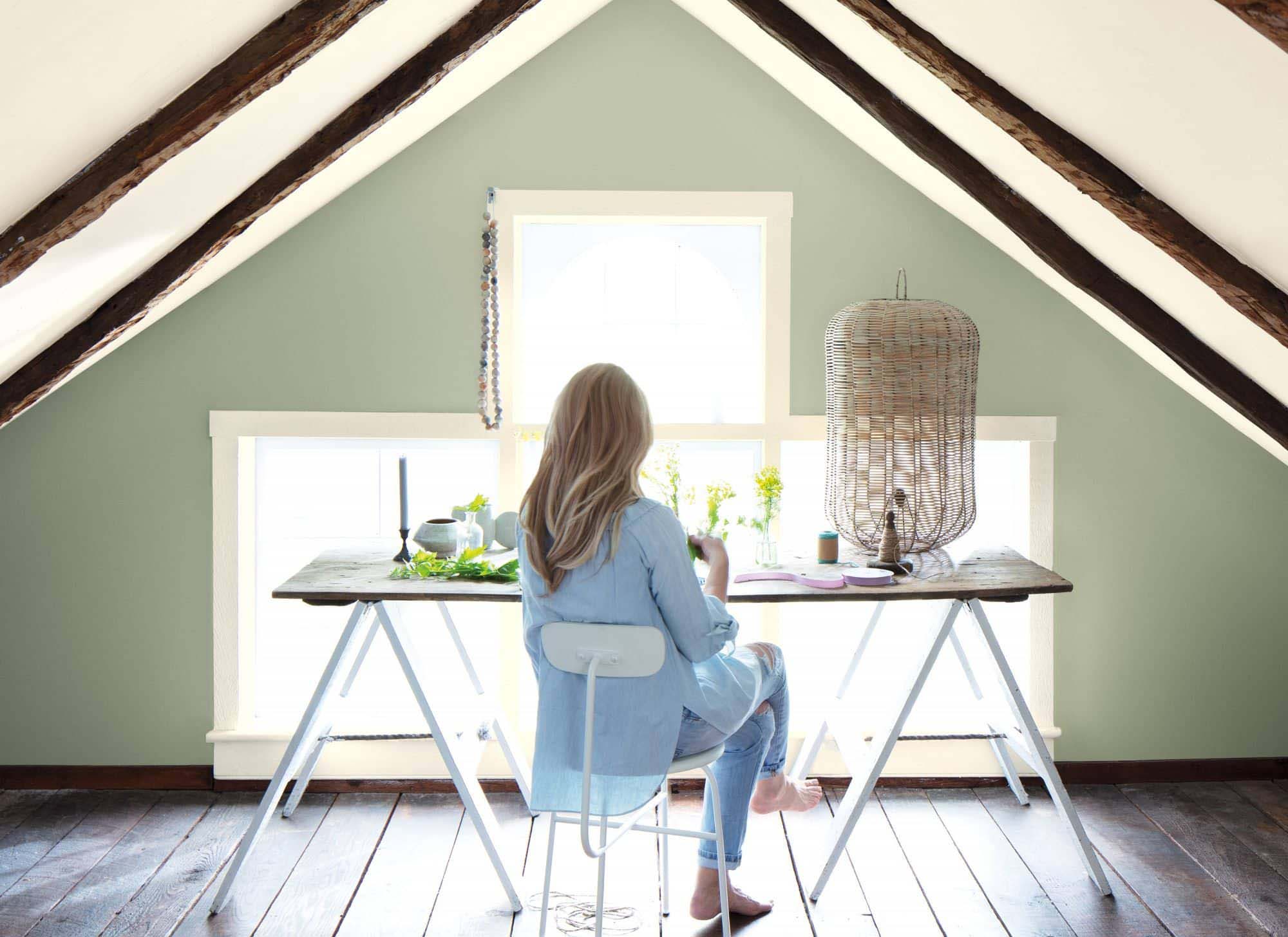 a woman sitting in an office upstairs with a sage green painted wall color.