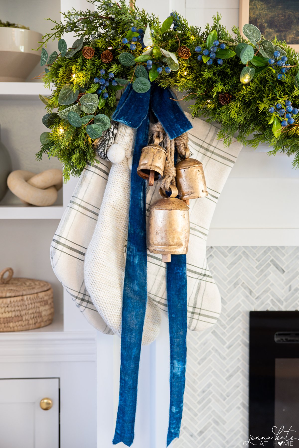 A close up picture of stockings with gold bells and blue ribbons hanging off the mantel.