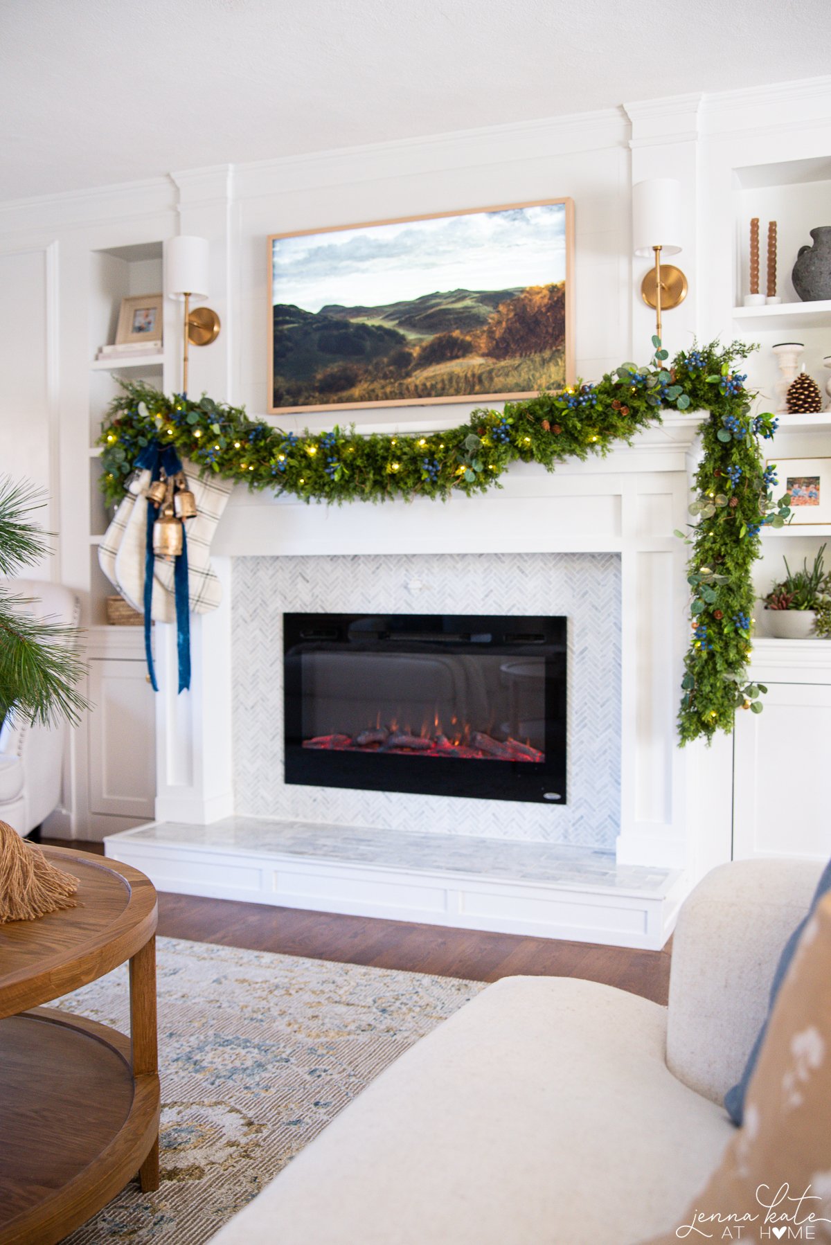 A view of the mantel decorated for Christmas with garland, stockings, and bells with a Frame TV hanging overhead.