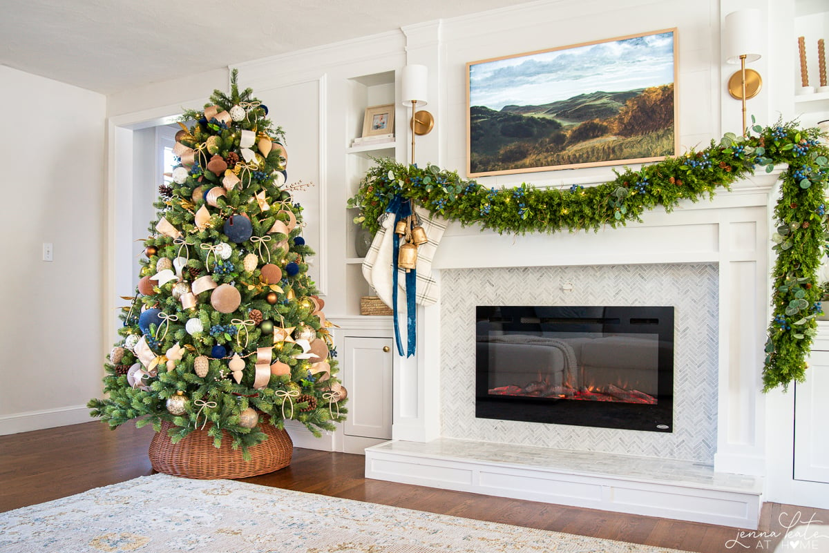 White fireplace with draping garland next to a decorated Christmas tree
