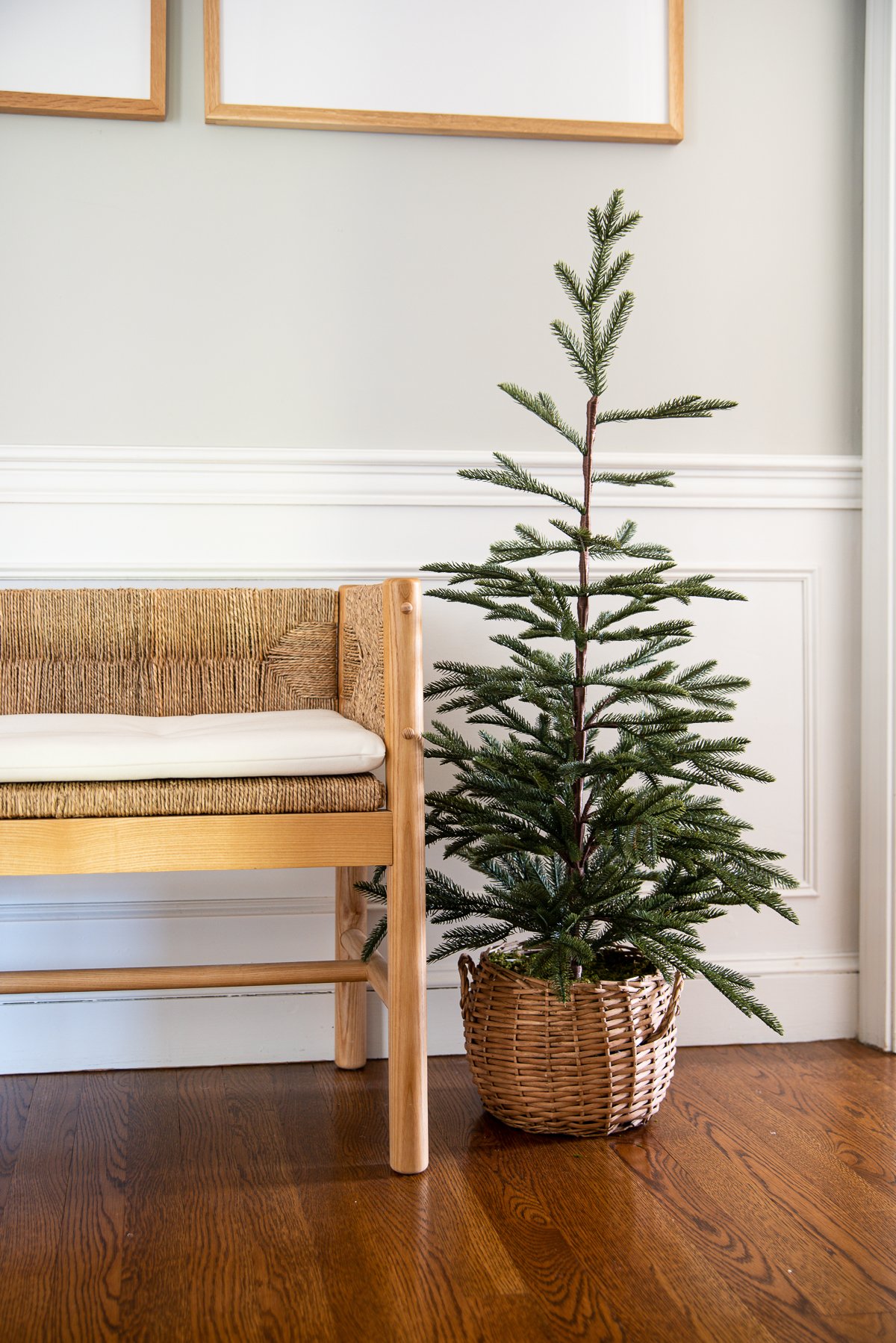 A small tree for Christmas in a woven basket sitting on the floor next to an entryway bench.