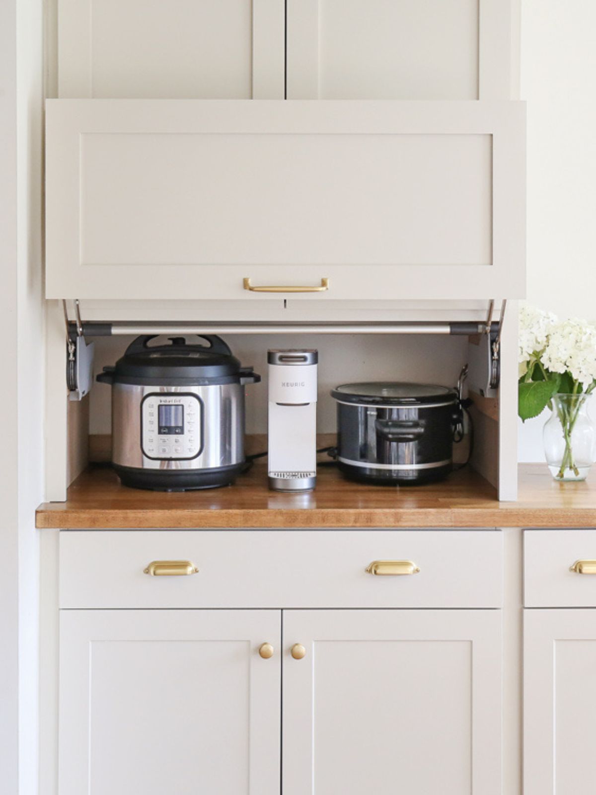 An appliance garage cabinet with a coffee maker, rice cooker, and crockpot stored inside.