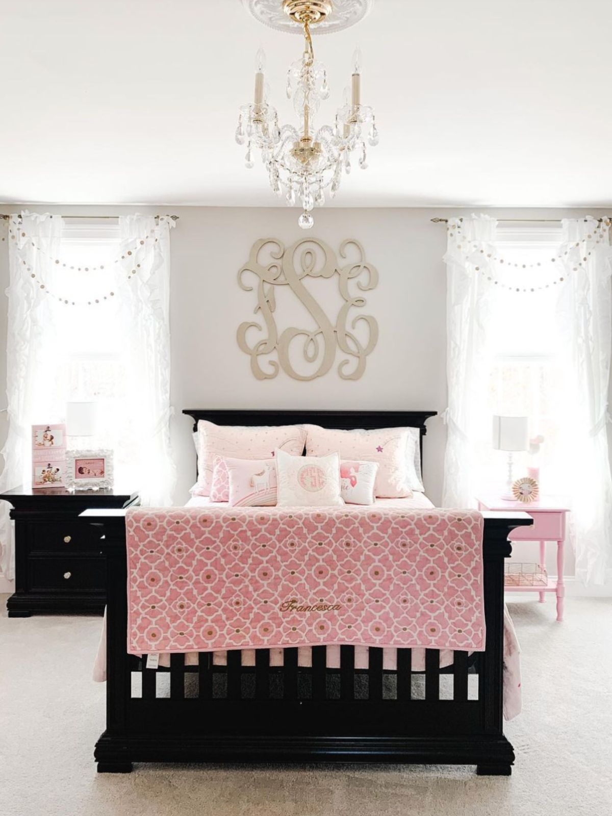A girl's bedroom painted with popular gray.  here's a black bed with pink bedding and a chandelier overhead.
