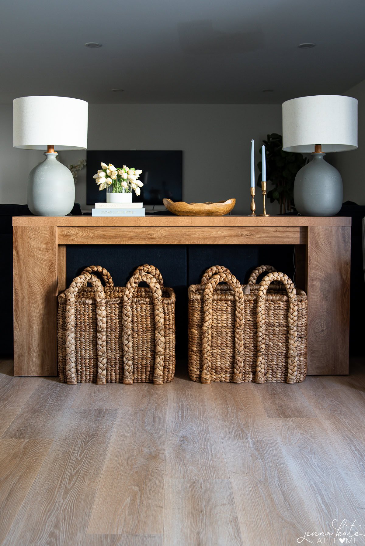 Styled console table behind a couch with tall lamps, faux tulips, baskets, decorative books, and coastal blue accents.